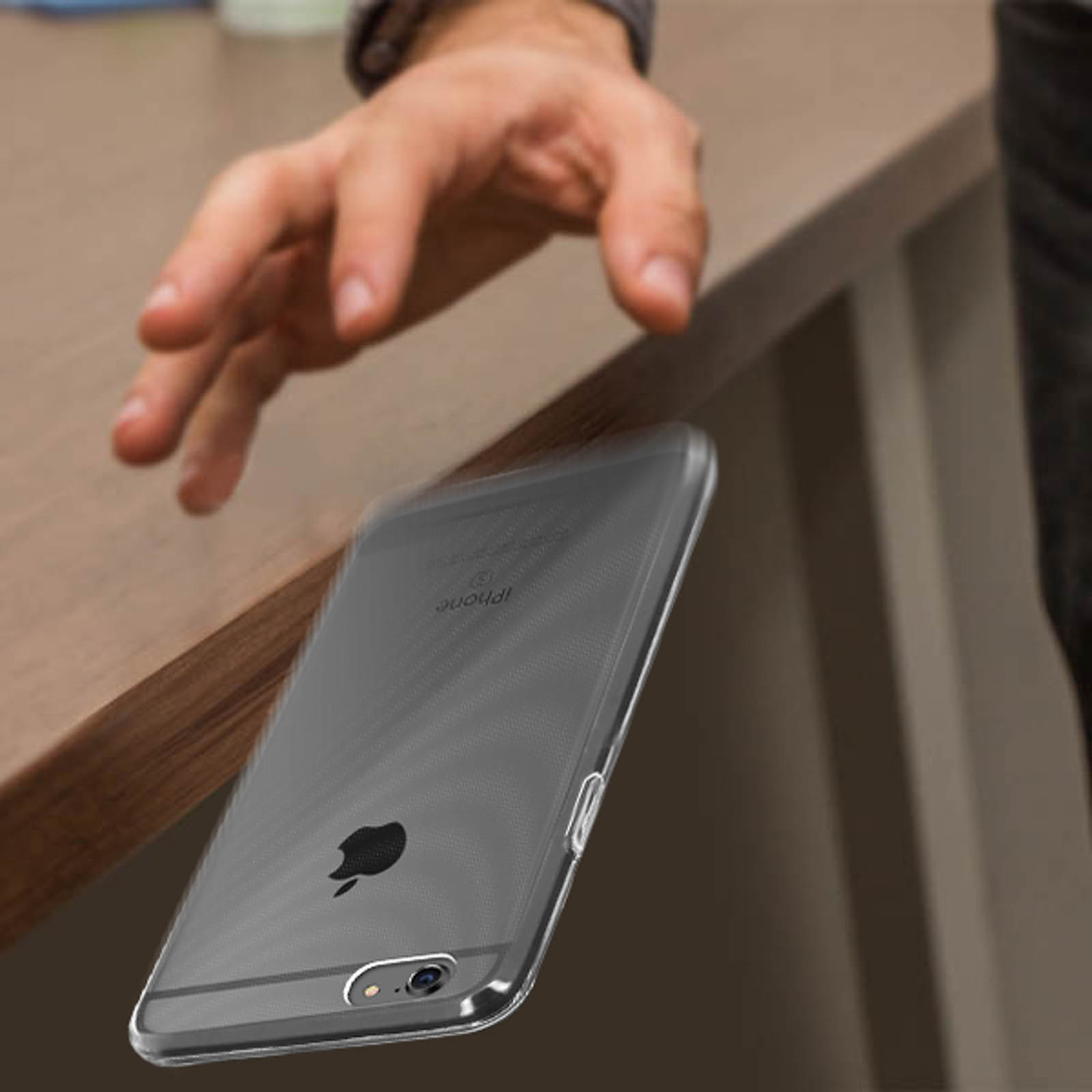 Un teléfono transparente con una funda transparente cayendo de una mesa. Una mano lo alcanza.