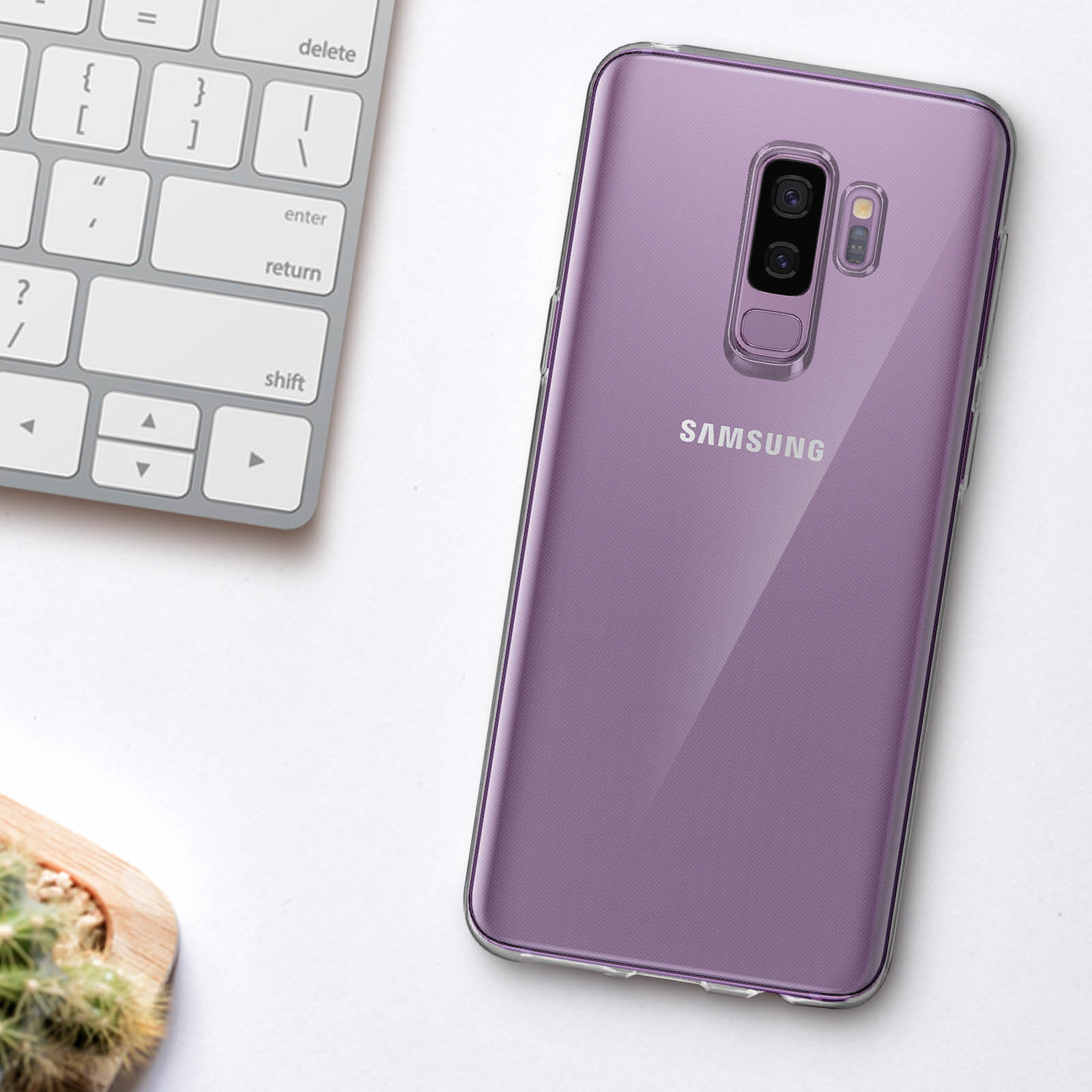 Telefono Samsung viola in una custodia trasparente, su una scrivania bianca accanto a una tastiera e un cactus.