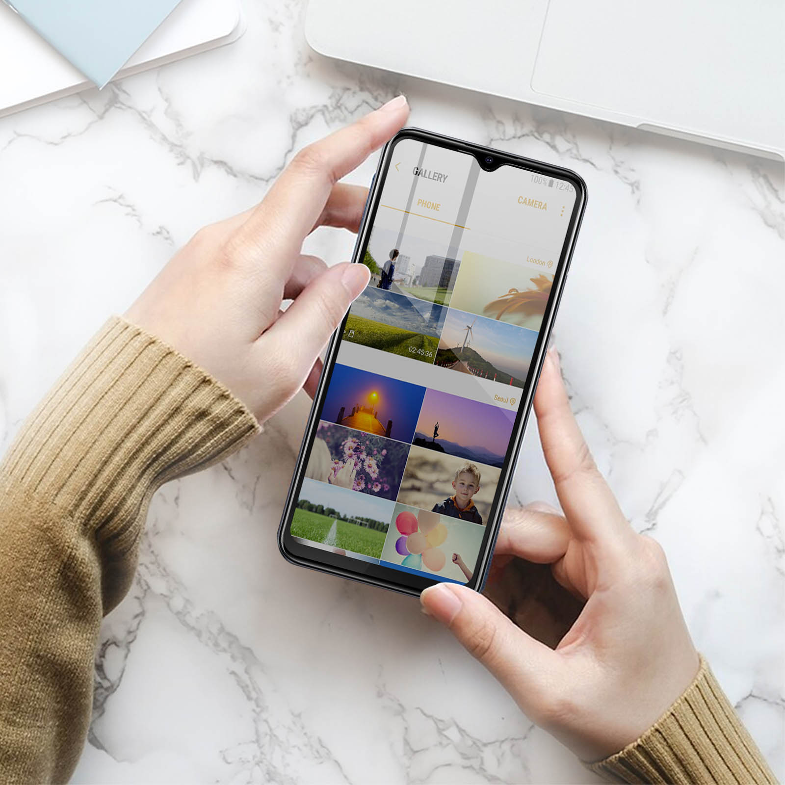 Mani che tengono uno smartphone che mostra una galleria di foto. Il telefono è appoggiato su una superficie di marmo.
