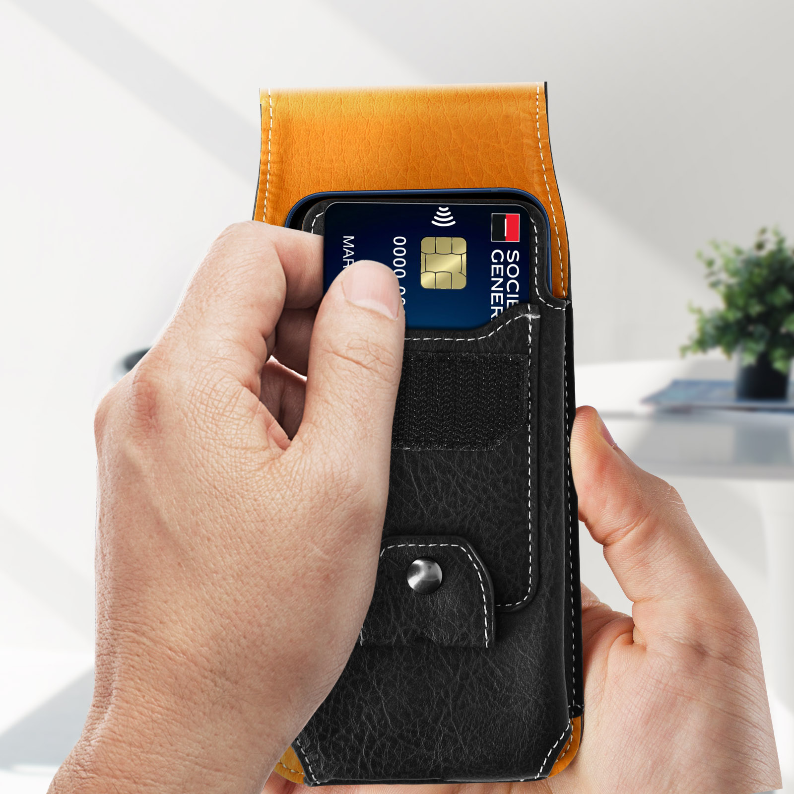 Una mano che tiene un telefono in una custodia nera e gialla, con una carta di credito visibile.