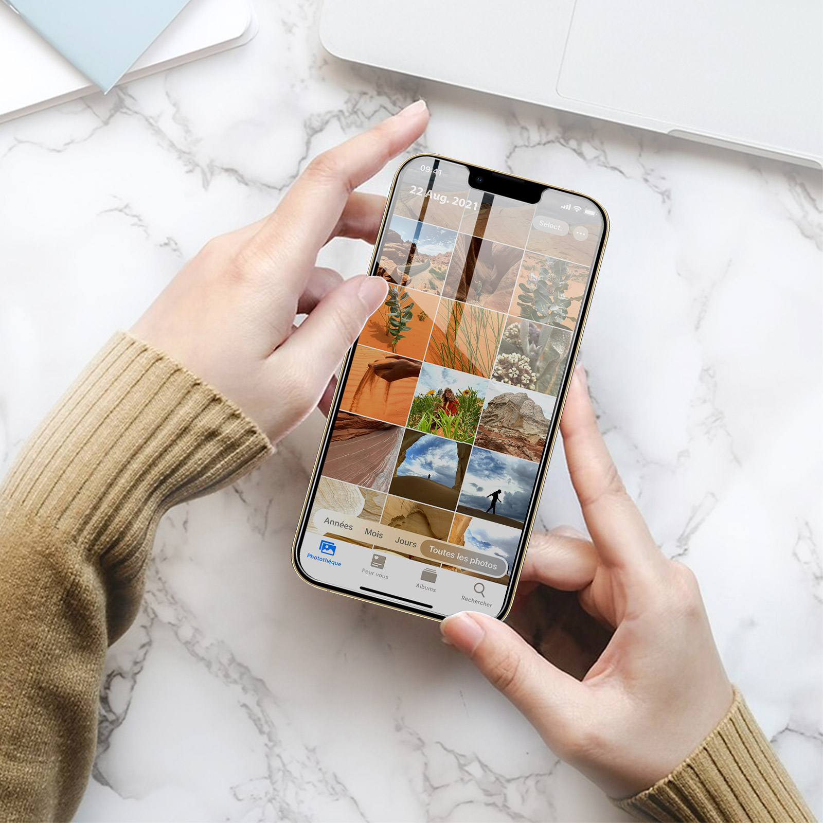 Mani che tengono un telefono d'oro, che mostra una galleria di foto con varie immagini su una superficie di marmo.