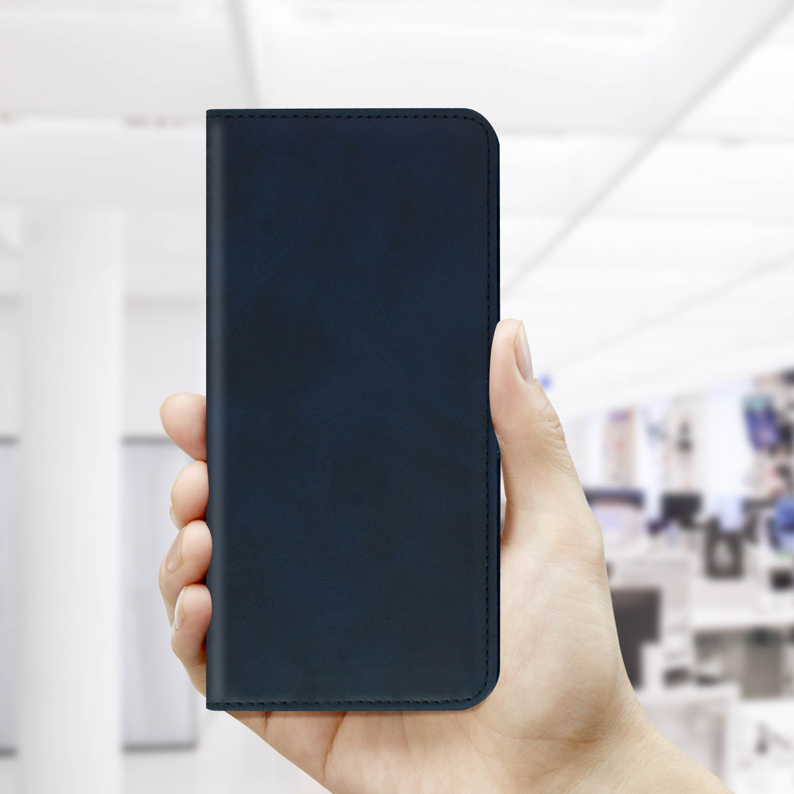 Een hand die een gesloten, donkerblauwe telefoonhoes vasthoudt tegen een wazige kantoorachtergrond.