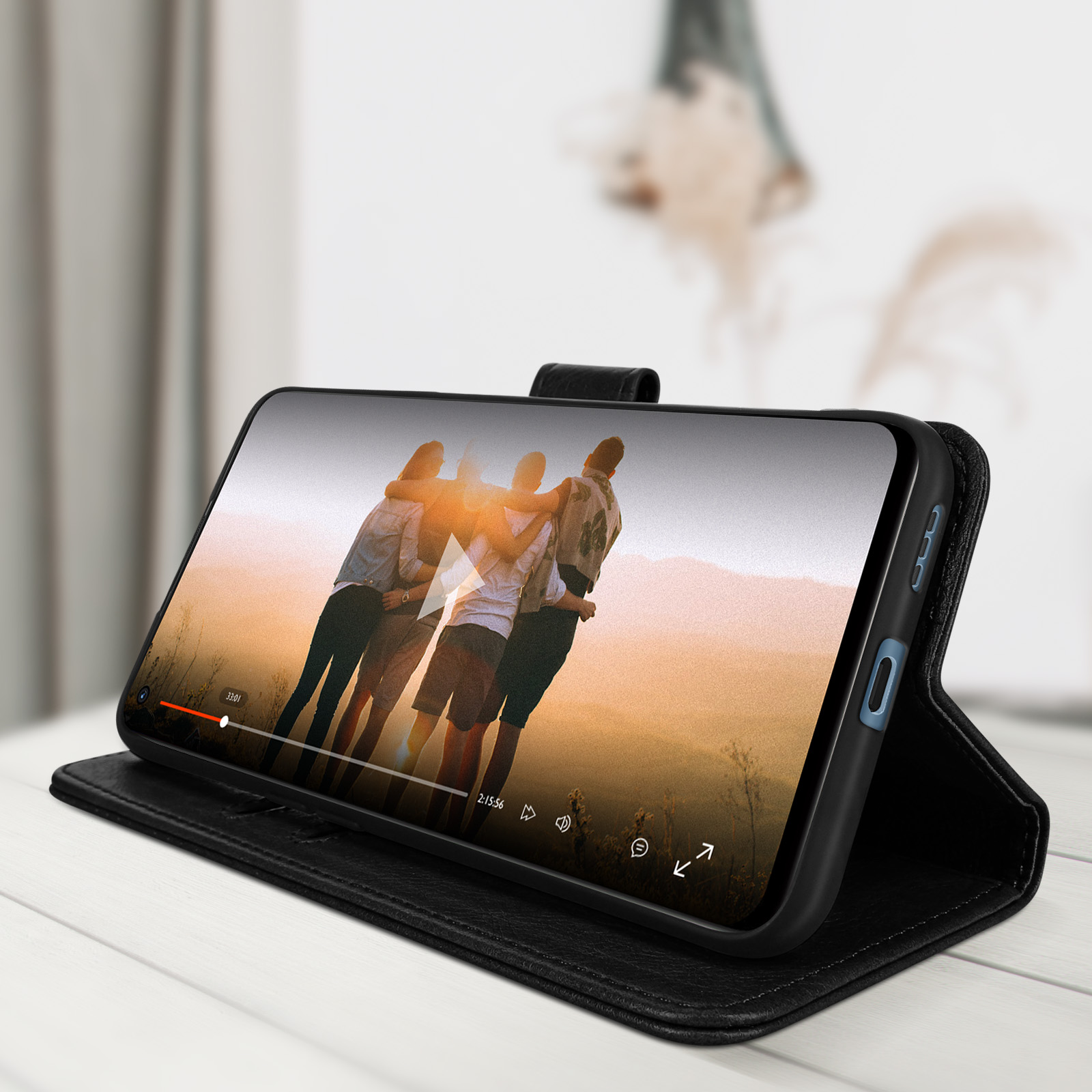 Een telefoon in een zwarte hoes toont een video van mensen die elkaar omhelzen tegen een zonsondergang.