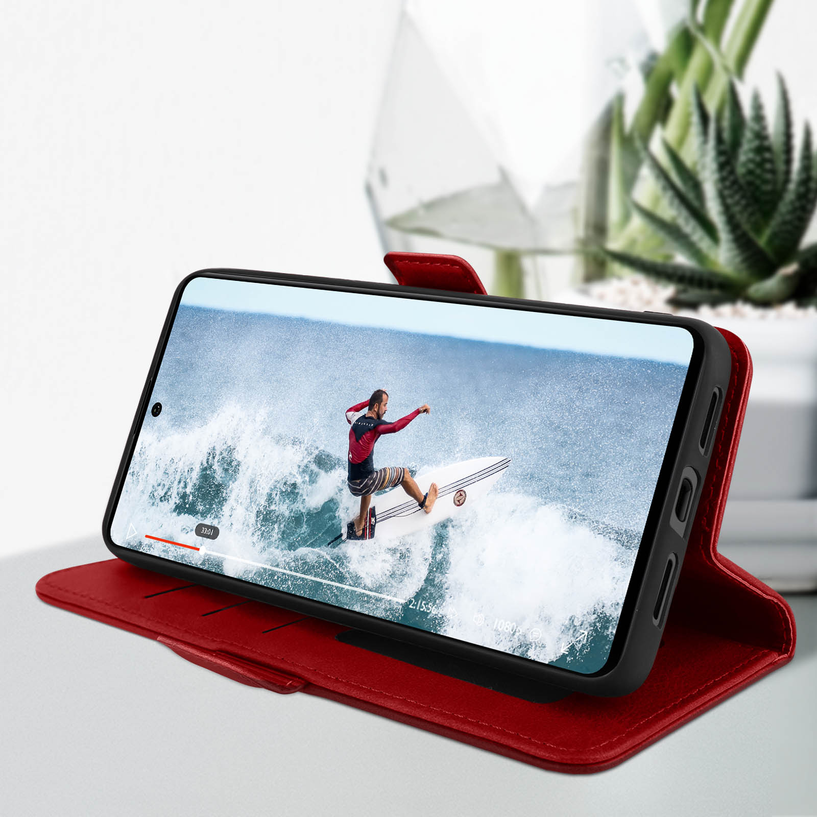 Telefoon met surfvideo in rode portemonnee. Een plant op de achtergrond.