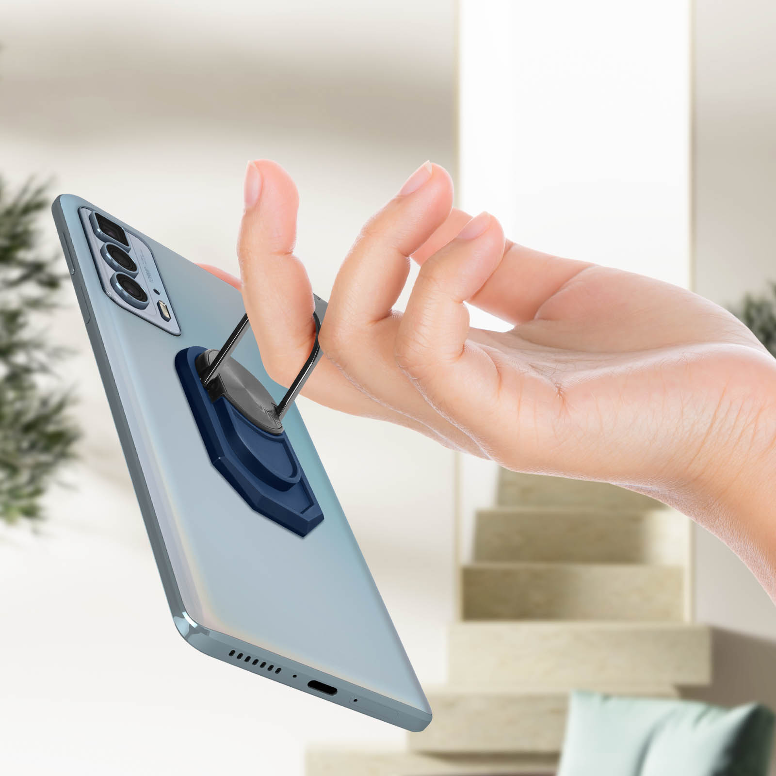 Mano che tiene un telefono con un supporto ad anello. Il telefono è argento e blu.