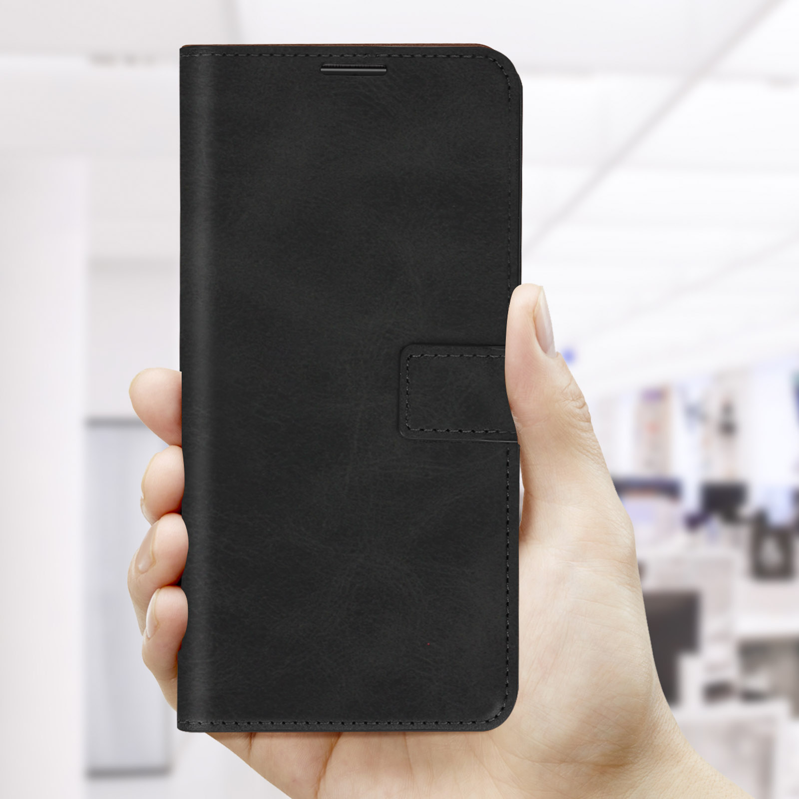 Main tenant un étui de téléphone noir fermé. Arrière-plan de bureau flou.
