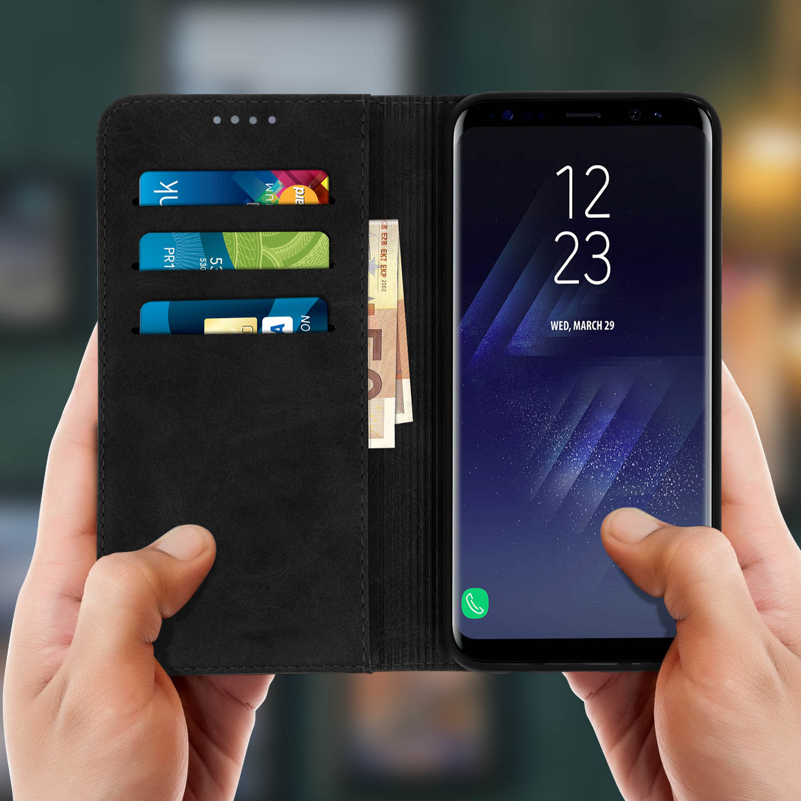 Mani che tengono una custodia nera per telefono con un telefono. La custodia ha scomparti per carte e contanti.