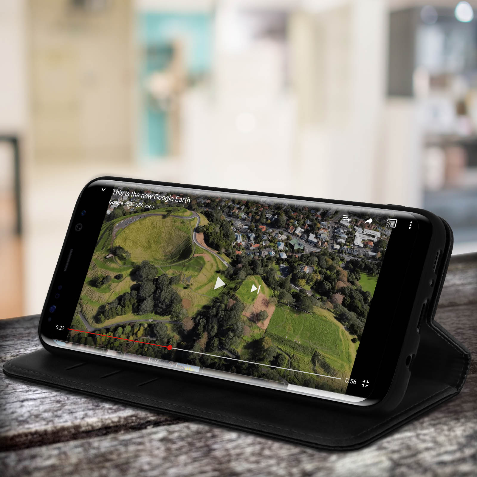 Telefono che mostra un video di mappa. Custodia nera. Tavolo di legno.