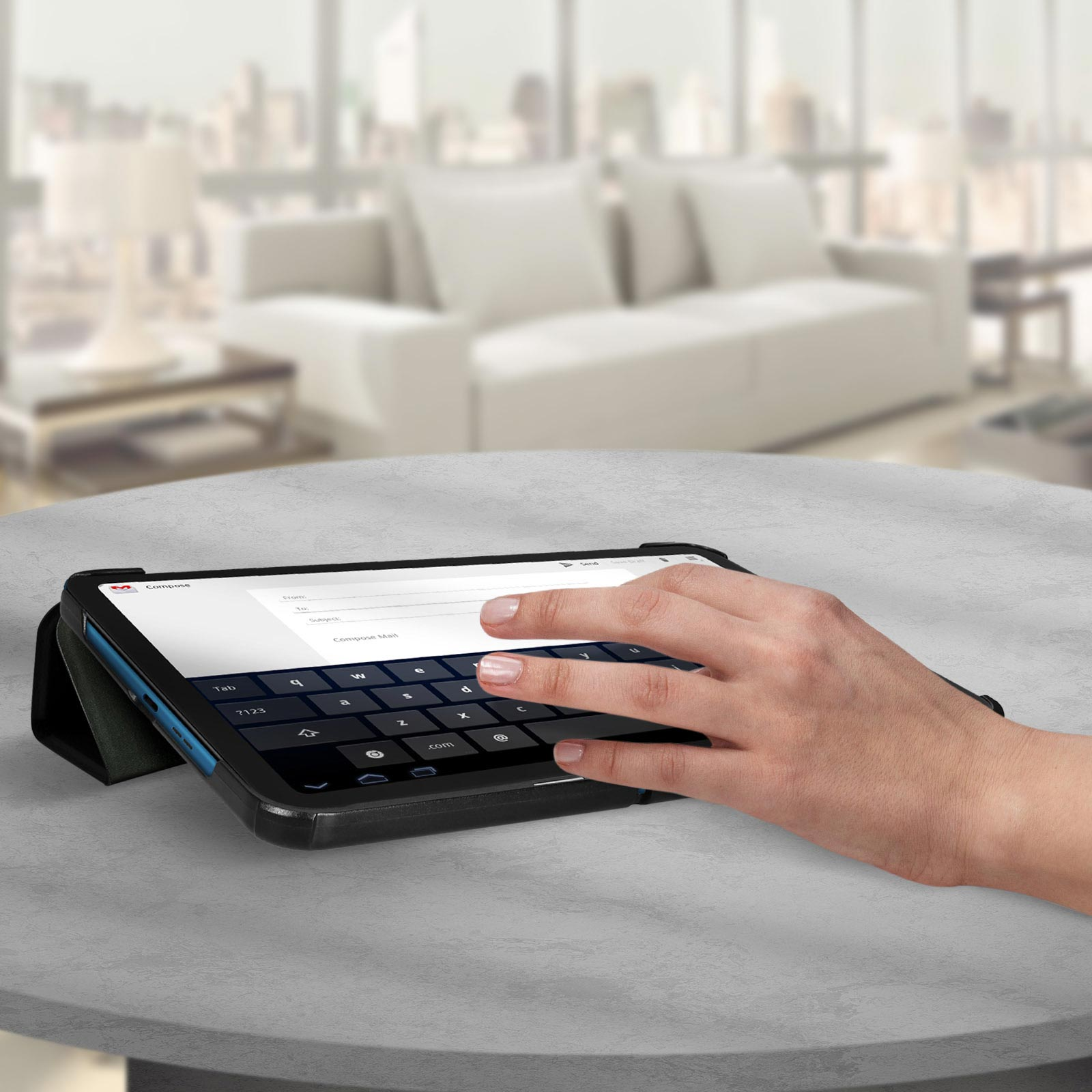 Mano che usa un tablet con tastiera su un tavolo. Sfondo: finestra e divano.