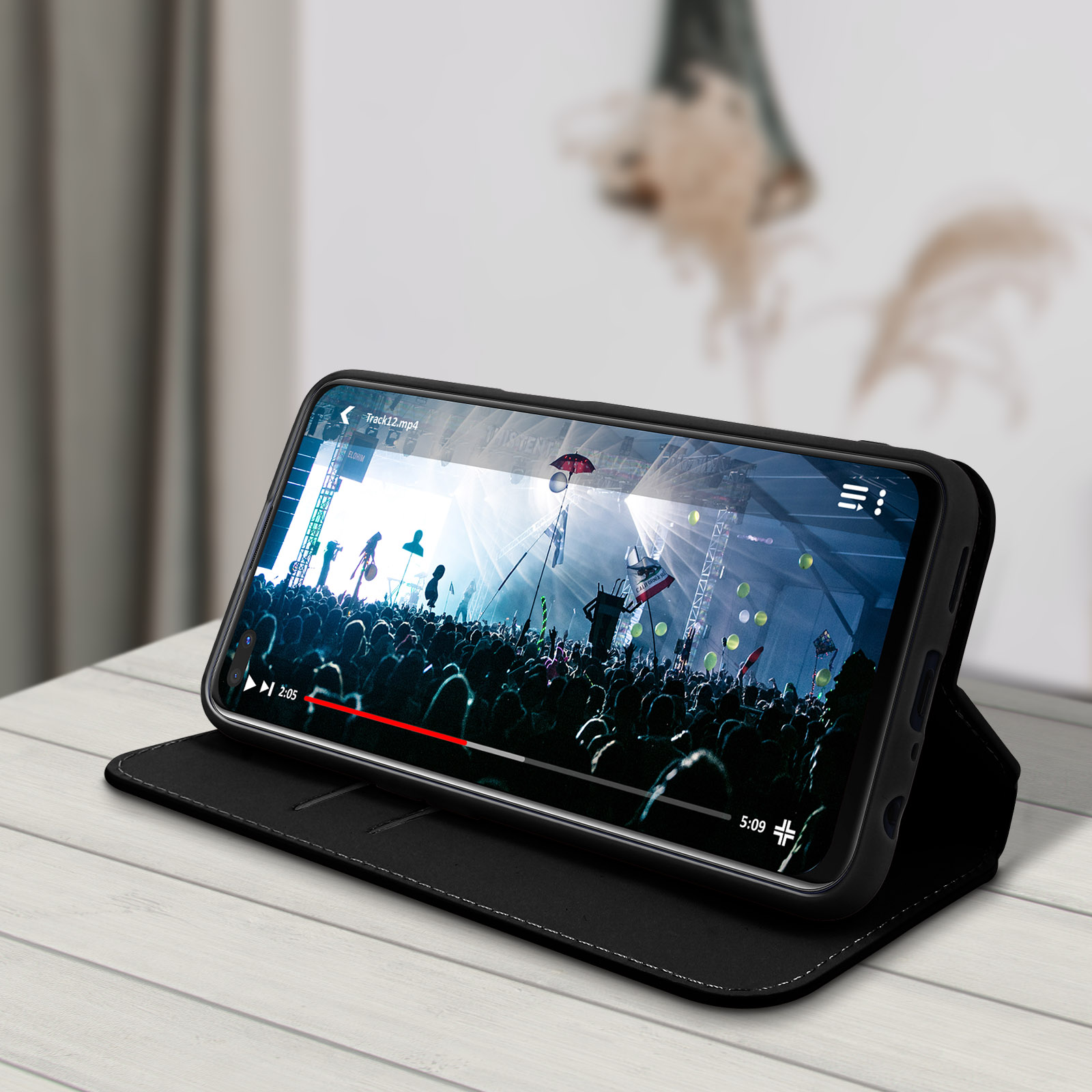 Un téléphone dans un étui noir joue une vidéo d'un concert. L'étui est sur une table blanche.