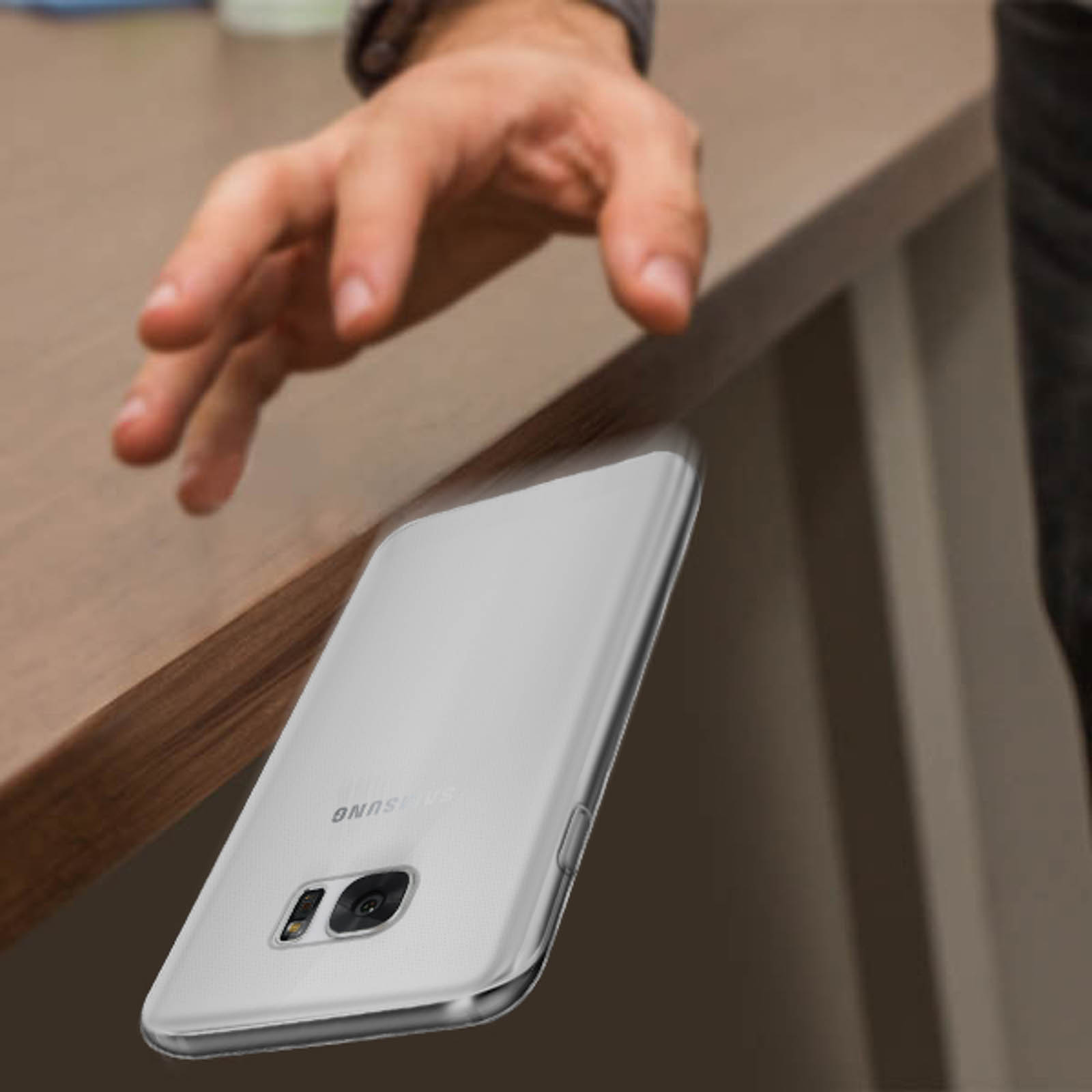 Hand schiebt Telefon vom Tisch, Telefon fällt, silberne Hülle sichtbar.