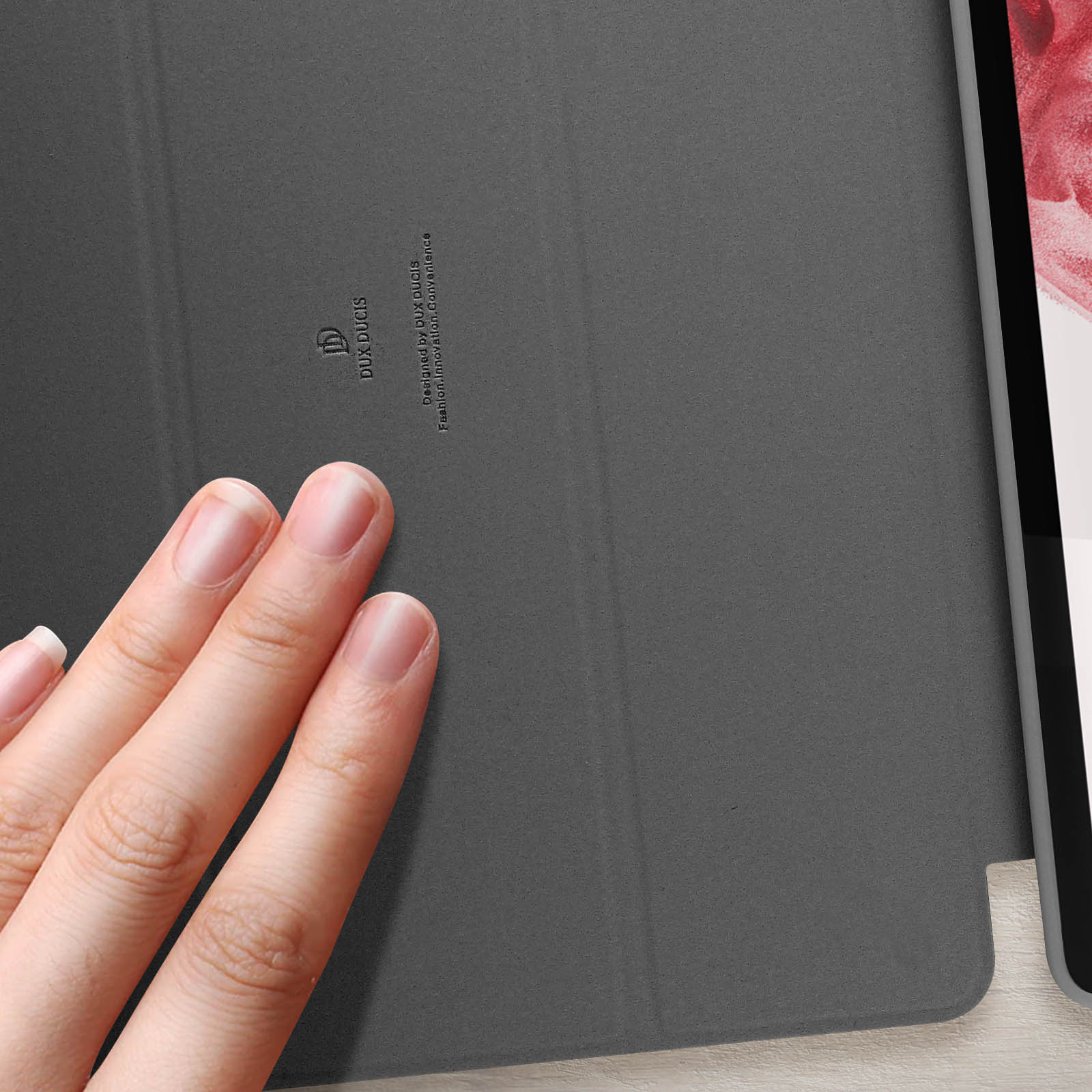 Una mano tocca una custodia grigia per tablet. La custodia ha il logo Dux Ducis e del testo.