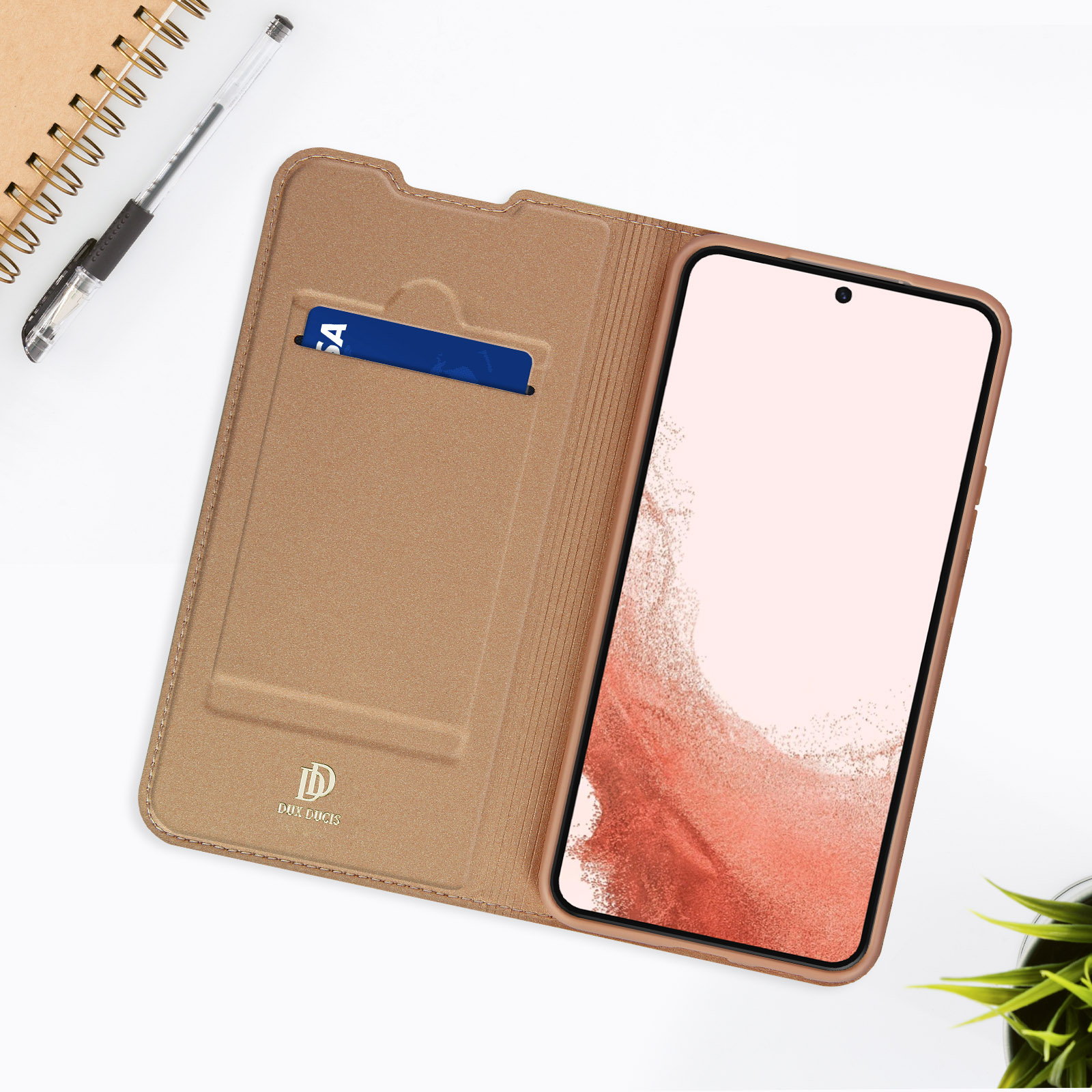 Telefono in custodia beige, carta di credito nella fessura, aperto con penna e pianta.