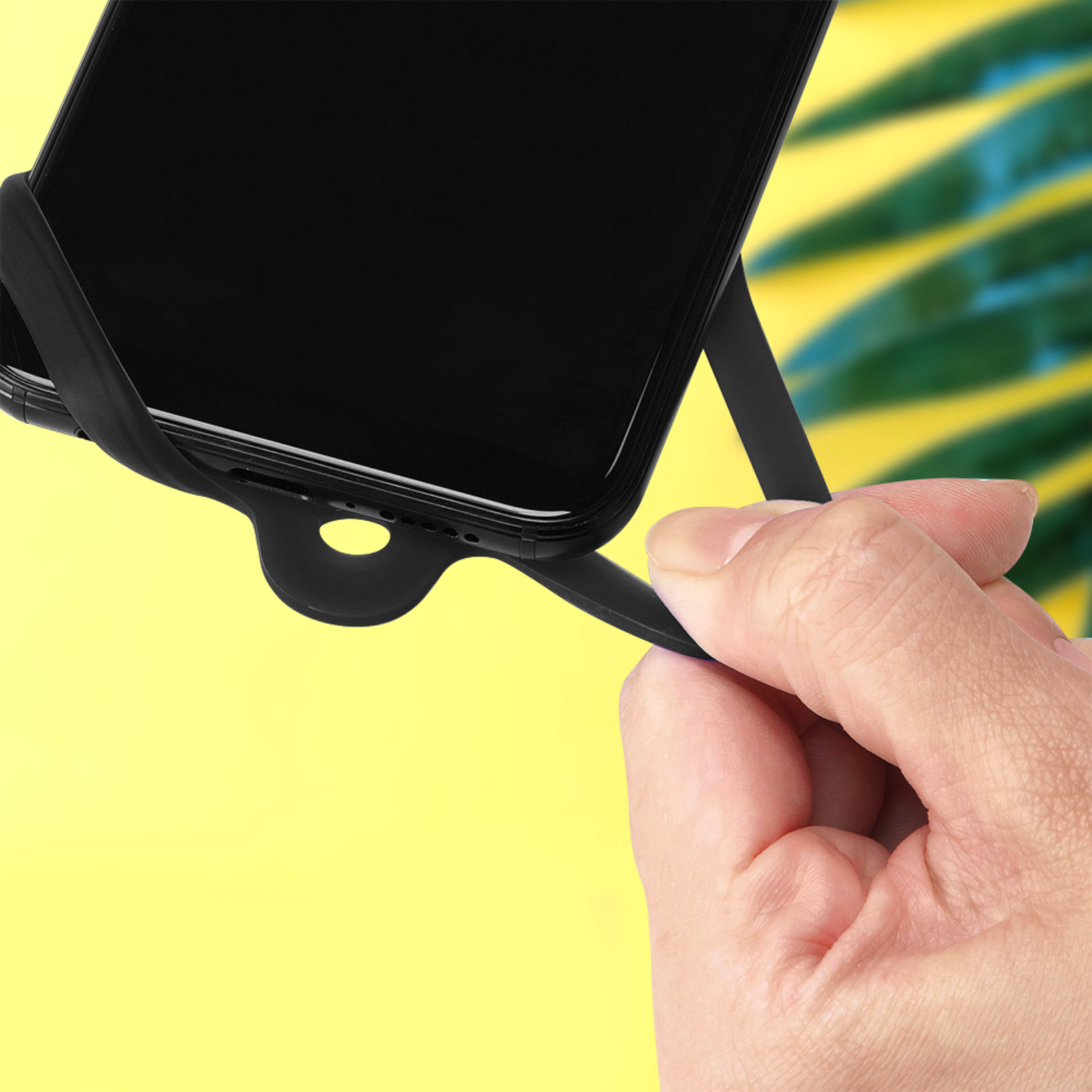 Una mano tiene un supporto nero per smartphone su sfondo giallo con foglie verdi.