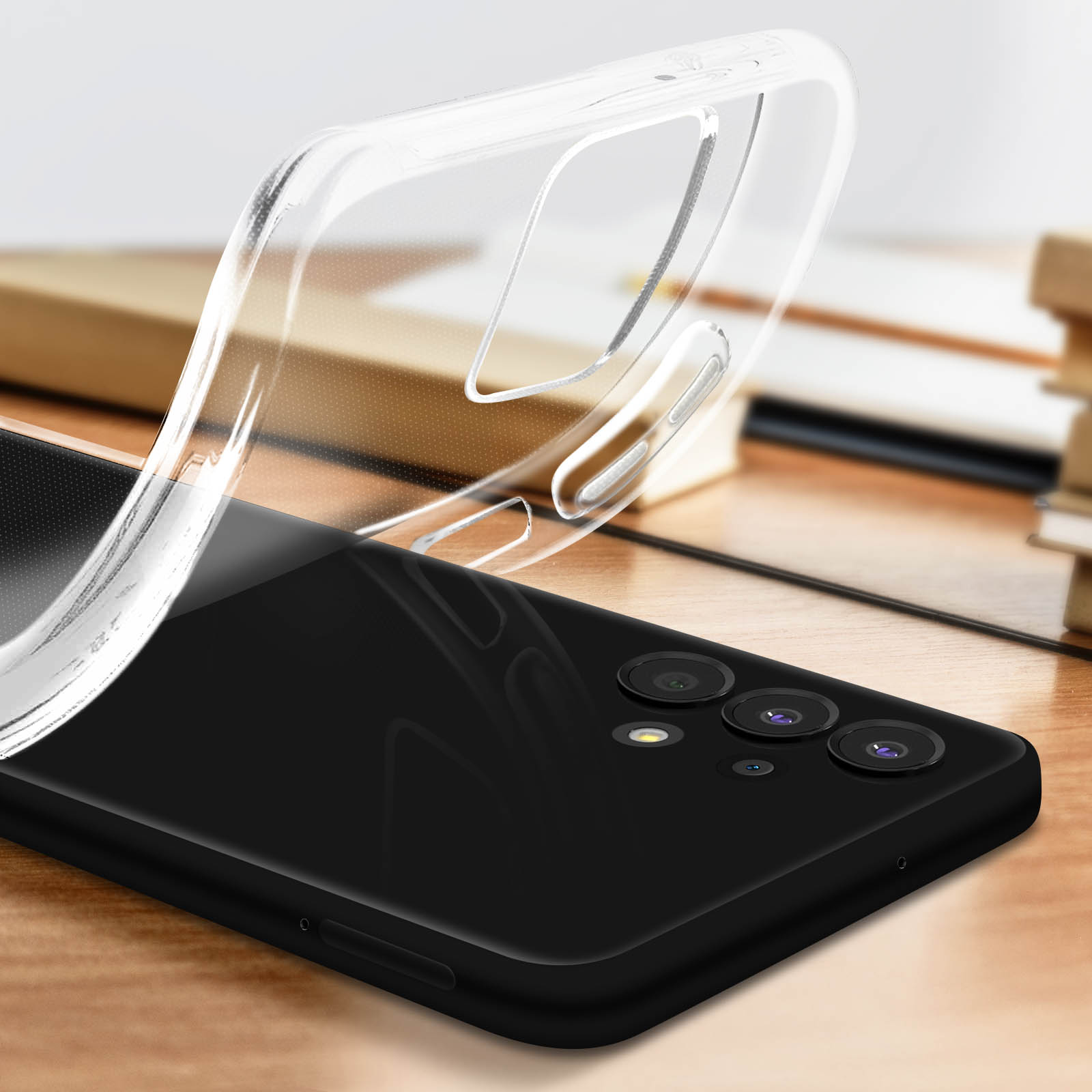 Una custodia trasparente viene sollevata sopra un telefono nero, appoggiato su un tavolo di legno con libri.