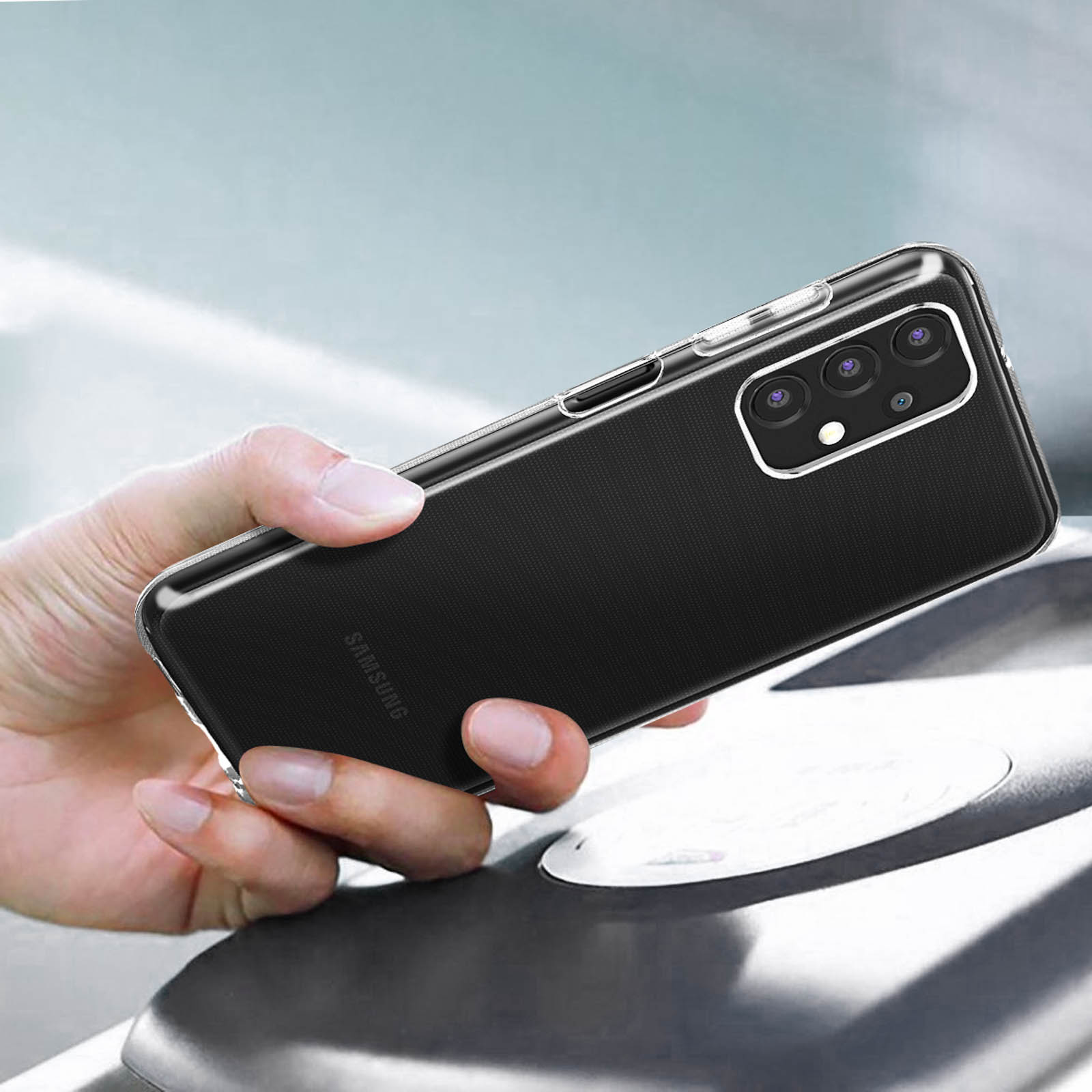 Mano che tiene un telefono con custodia trasparente. Il telefono ha tre fotocamere.