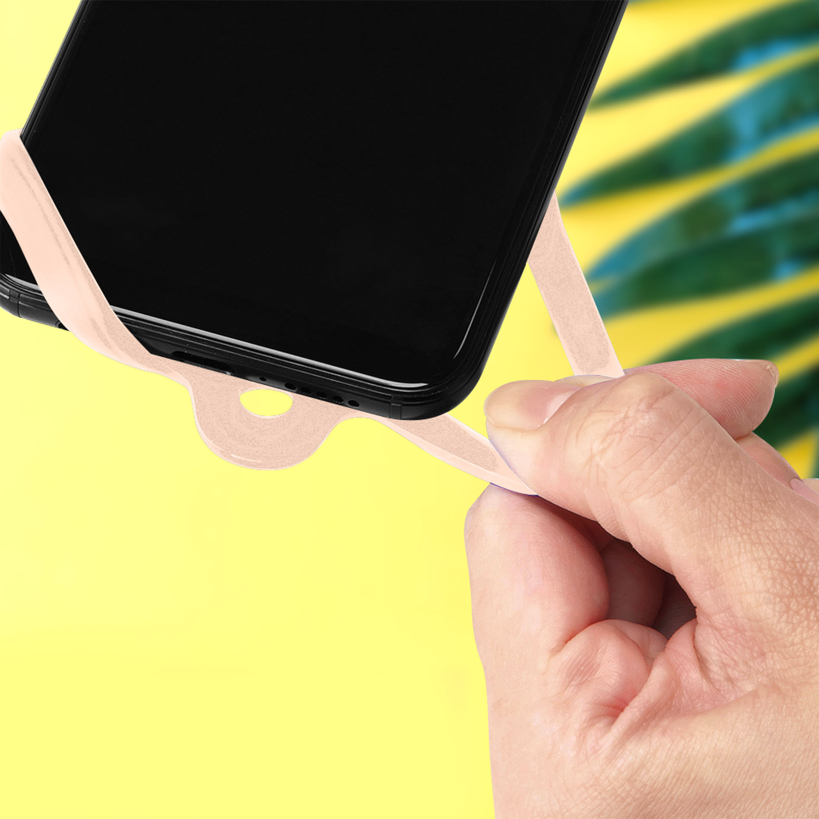 Una mano tiene un telefono con cinturino rosa. Sfondo giallo.