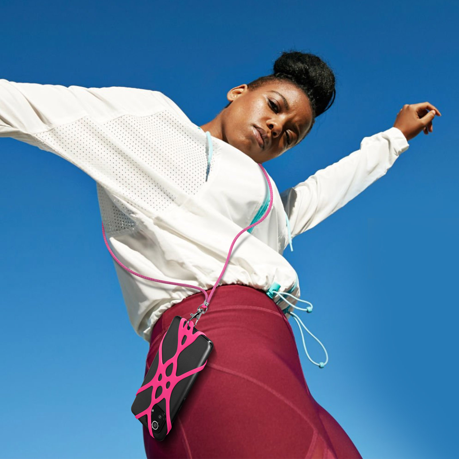 Una donna con una giacca bianca e leggings rossi, che tiene un telefono con un cinturino rosa.