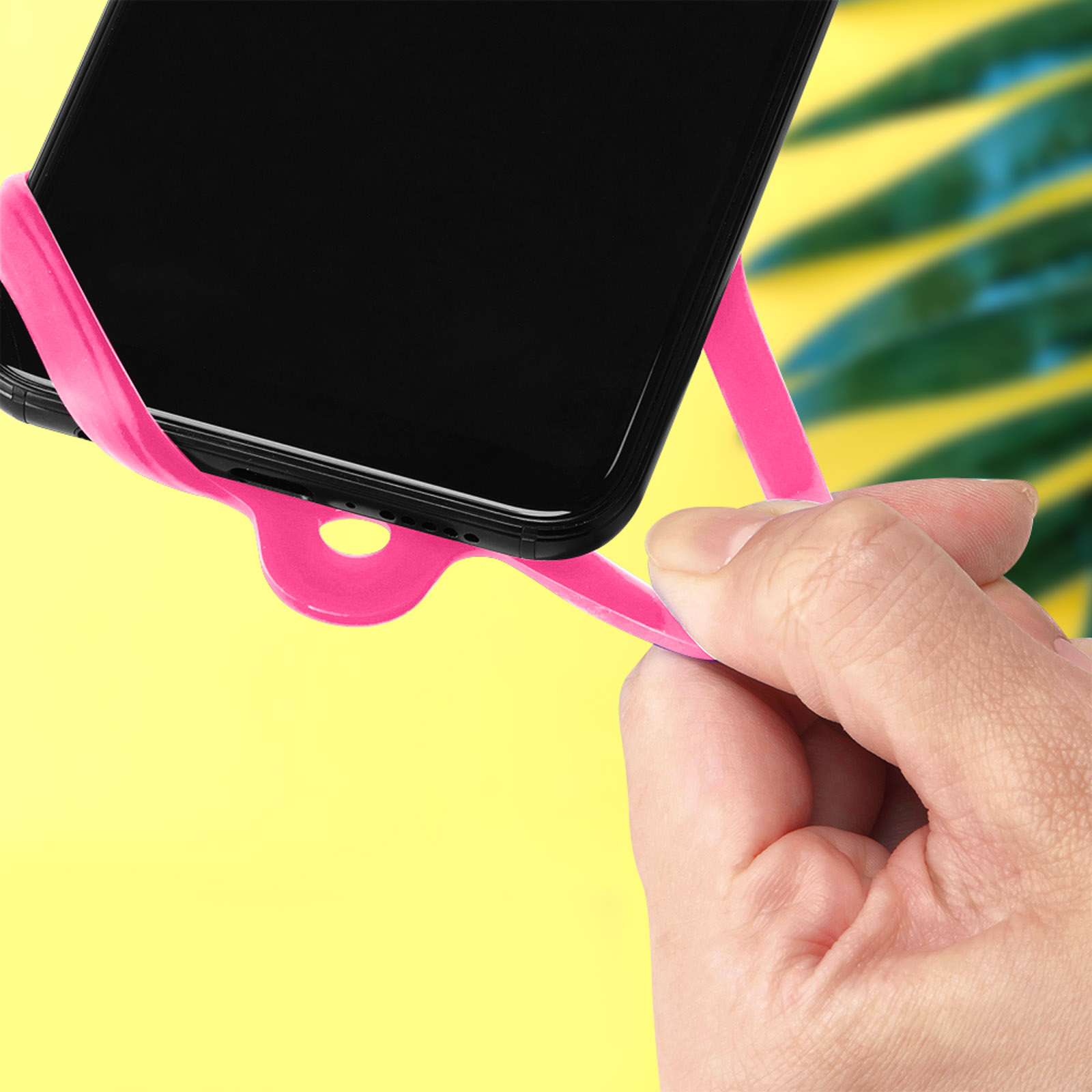 Una mano che tiene un telefono con un cinturino rosa, su sfondo giallo. Il telefono è nero.