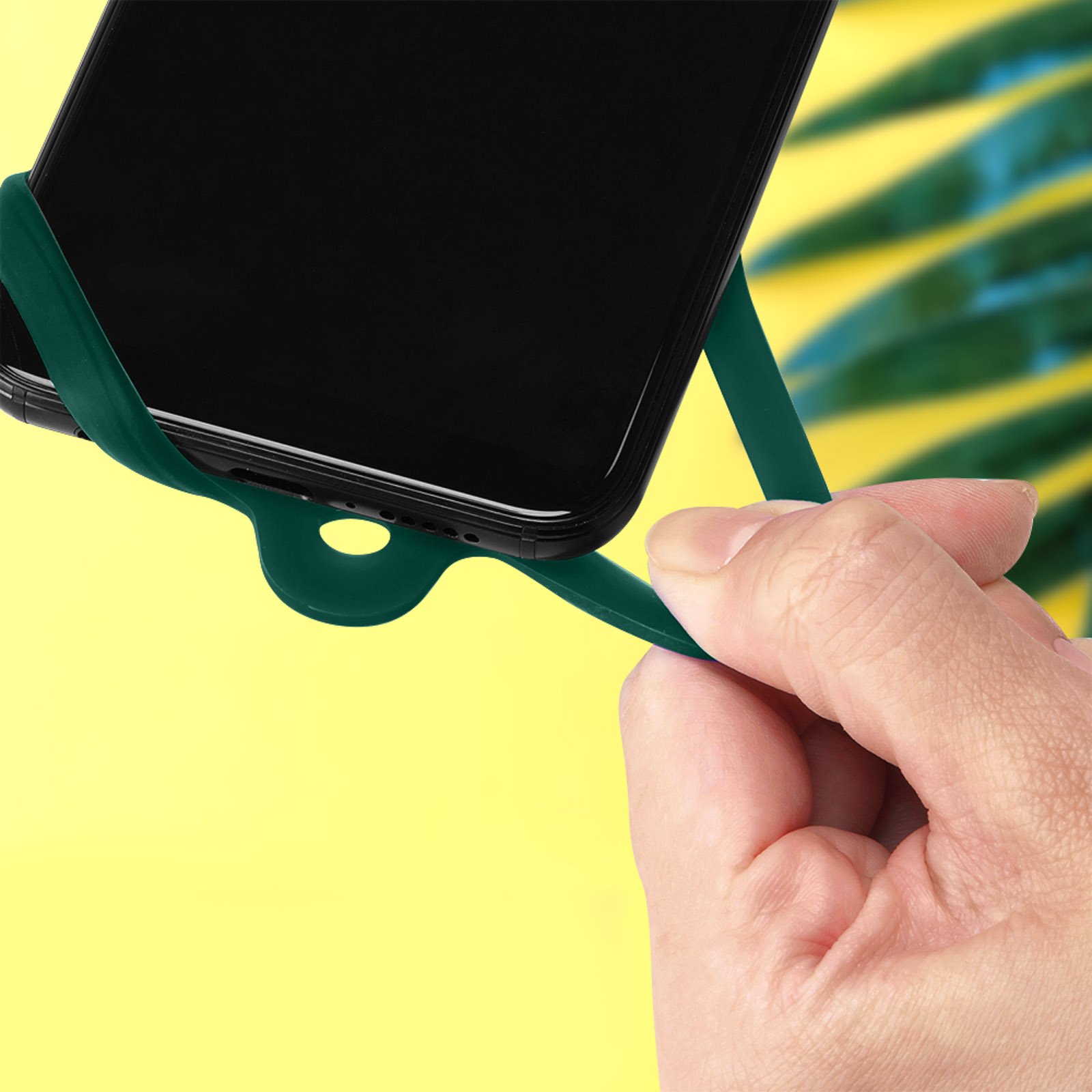 Una mano tiene un anello verde scuro attaccato a uno smartphone su sfondo giallo.