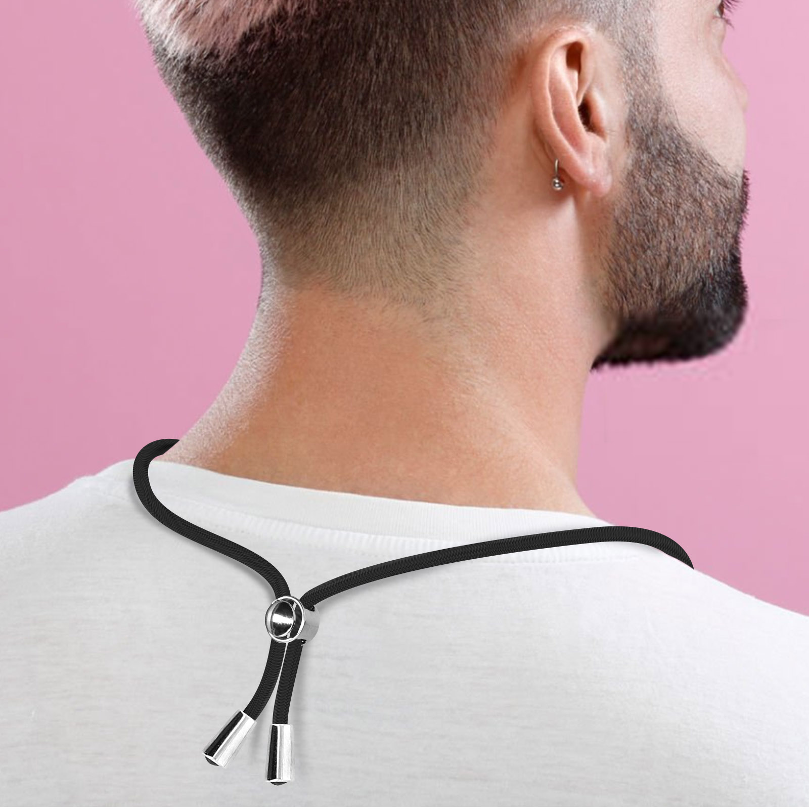 Vista posteriore di un uomo con taglio corto e barba, indossa una maglietta bianca e una collana di corda nera.
