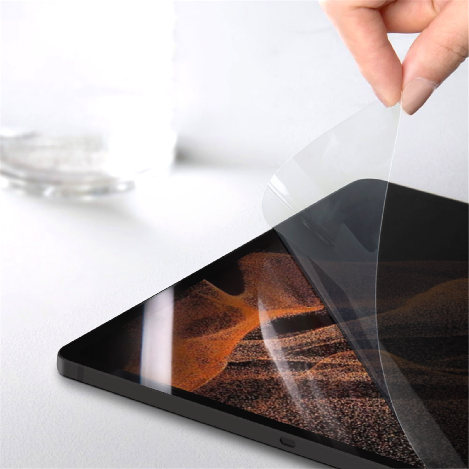 Una mano che stacca una protezione per lo schermo da un telefono o tablet. La superficie è bianca.