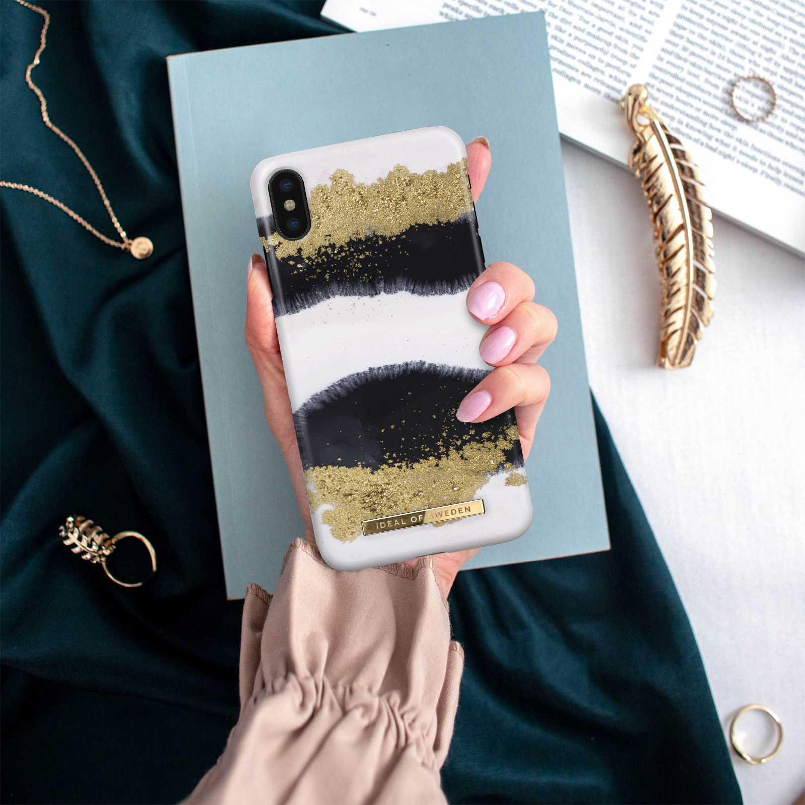Person hält Telefon mit gold-schwarzer Hülle und Accessoires.