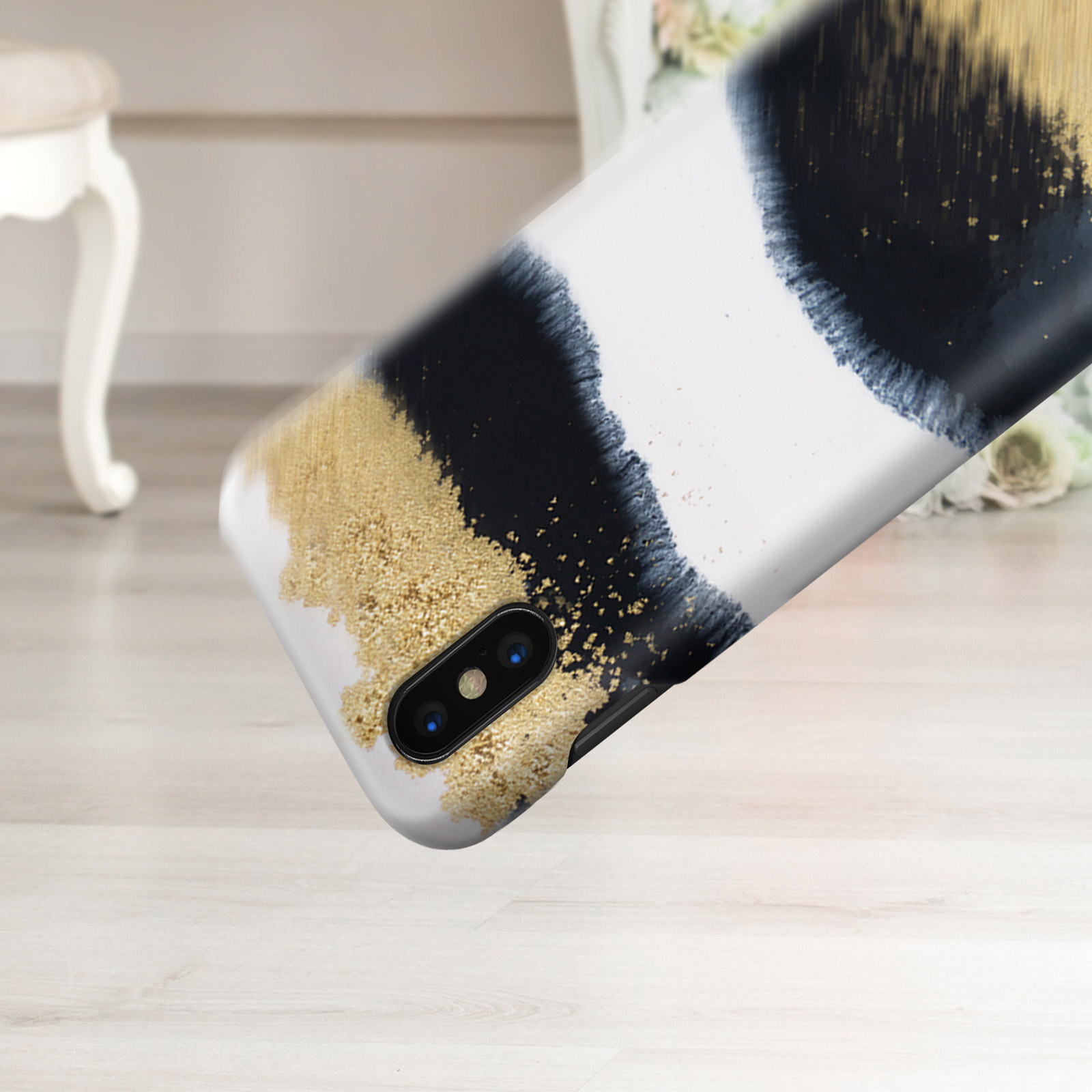 Eine Handyhülle mit schwarzer und goldener Farbe. Der Hintergrund ist ein weißer Holzboden.