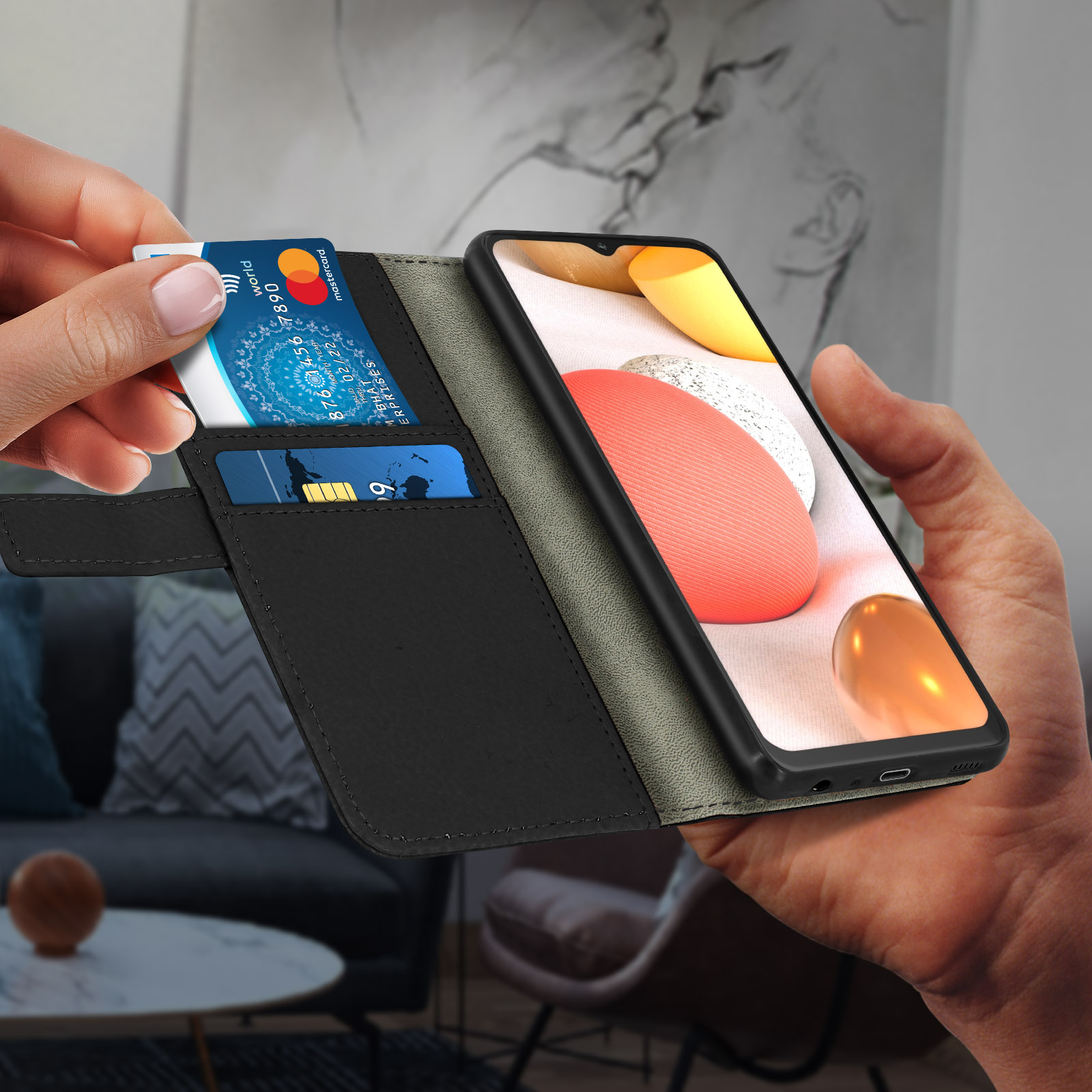 Mano inserisce carta di credito in custodia nera con telefono, ambientazione salotto.