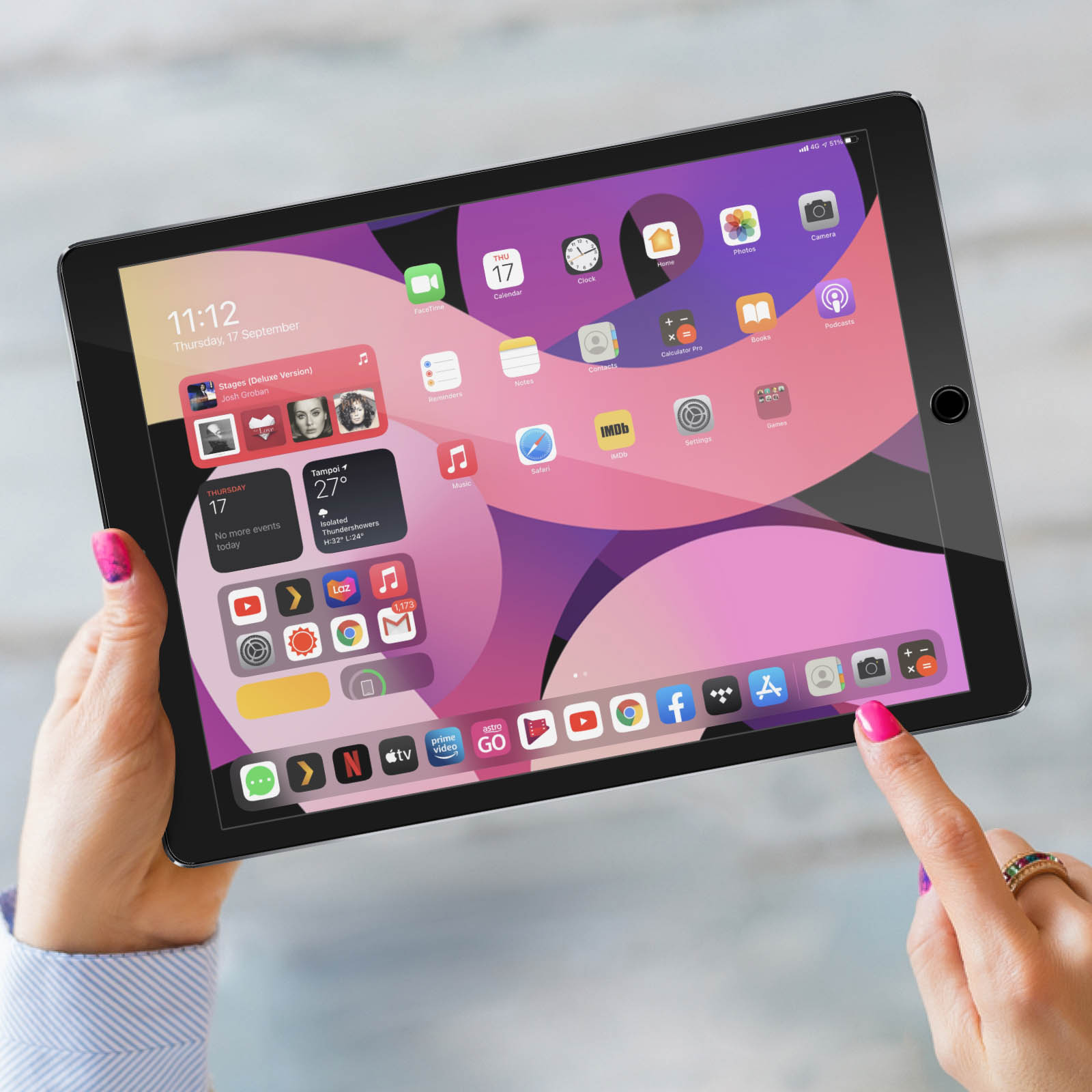 Le mani di una donna che tengono un tablet che mostra la schermata iniziale con varie app e widget.