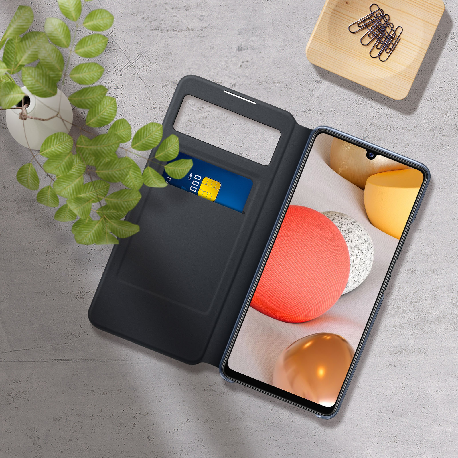 Un teléfono en una funda azul está en una funda abierta. Una tarjeta de crédito está en la funda. Sobre una superficie gris.