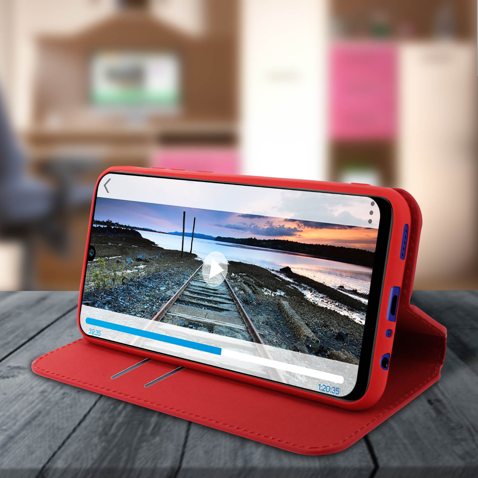 Una custodia rossa per telefono contiene un telefono che mostra un video di un binario. La custodia è aperta su una superficie di legno.