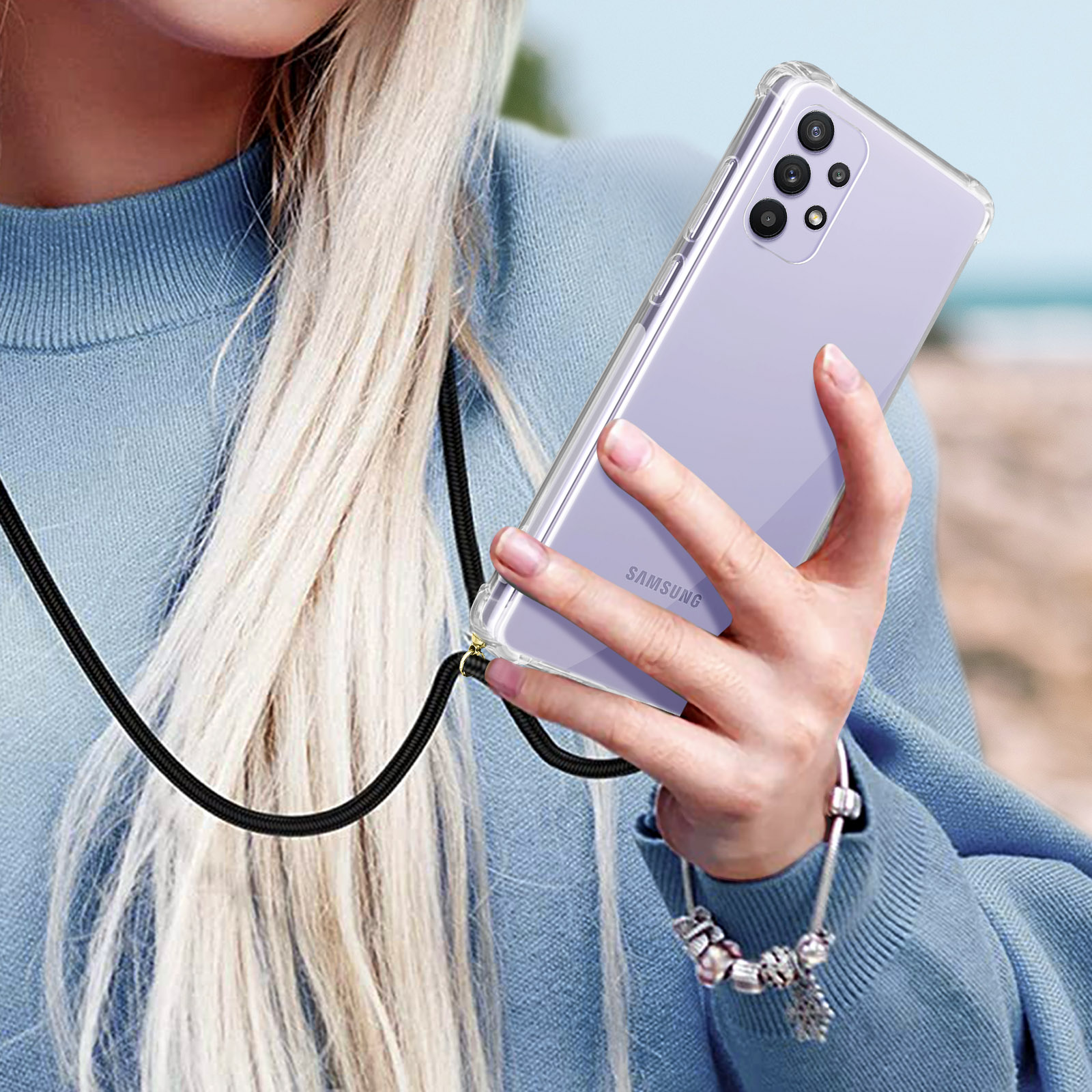 Donna che tiene un telefono con una custodia trasparente e un cordino nero. Sfondo sfocato.