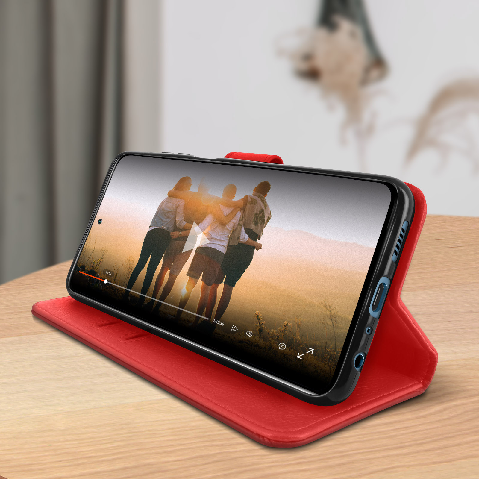 Telefoon in rode hoes, opgezet, met een video van mensen op een wazige achtergrond.