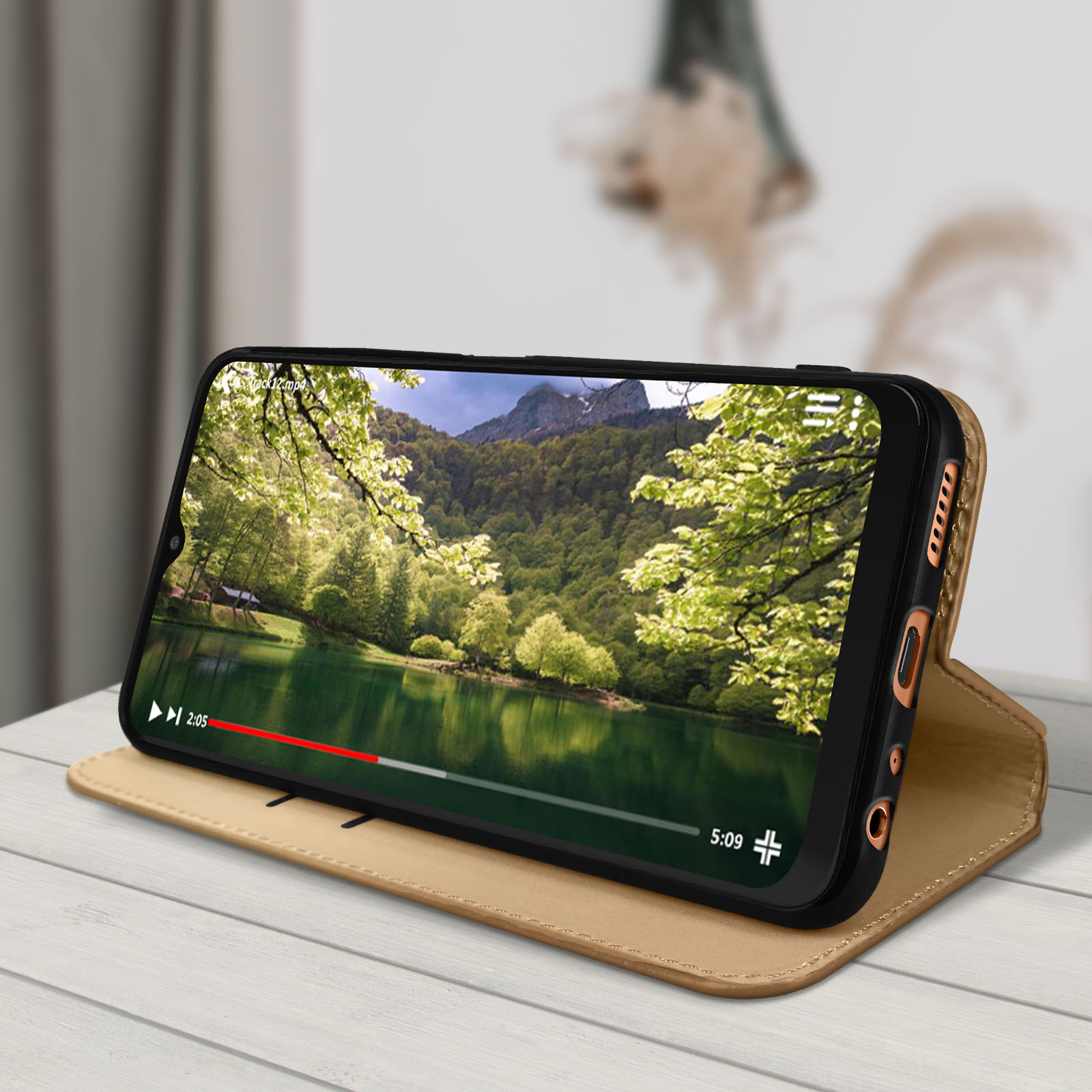 Telefoon in beige hoesje toont landschapsvideo. Hoesje open, op tafel. Achtergrond is wazig.