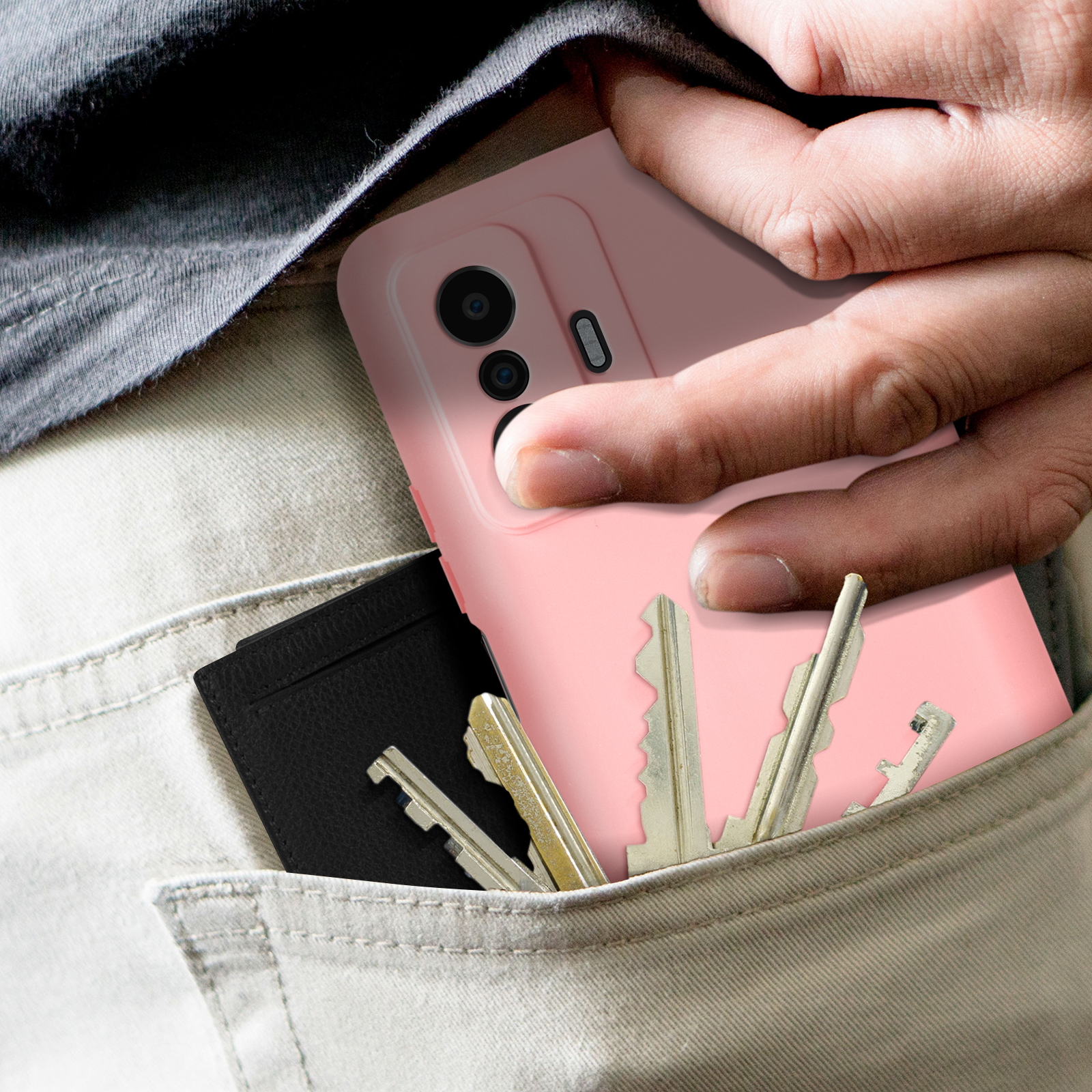 Mano in tasca con telefono in custodia rosa, chiavi e portafoglio nero. Sfondo: tasca dei pantaloni grigi.