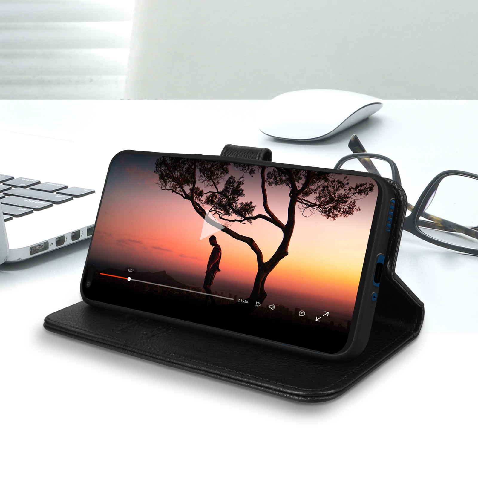 Telefoon in een zwarte leren hoes, met een video van een boom bij zonsondergang. Een muis en bril liggen op het bureau.