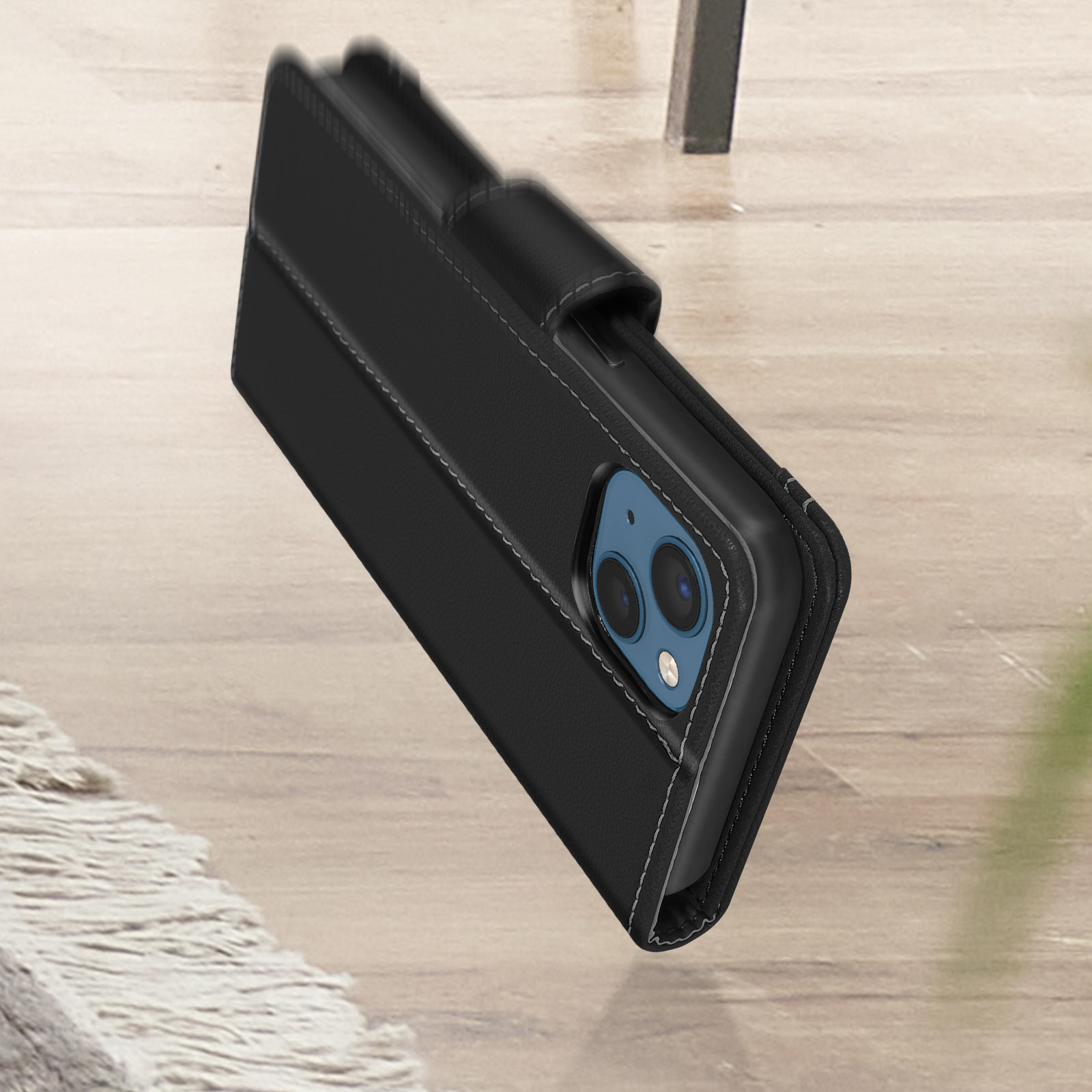 Un téléphone noir dans un étui en cuir noir avec des coutures blanches, posé sur une surface en bois.
