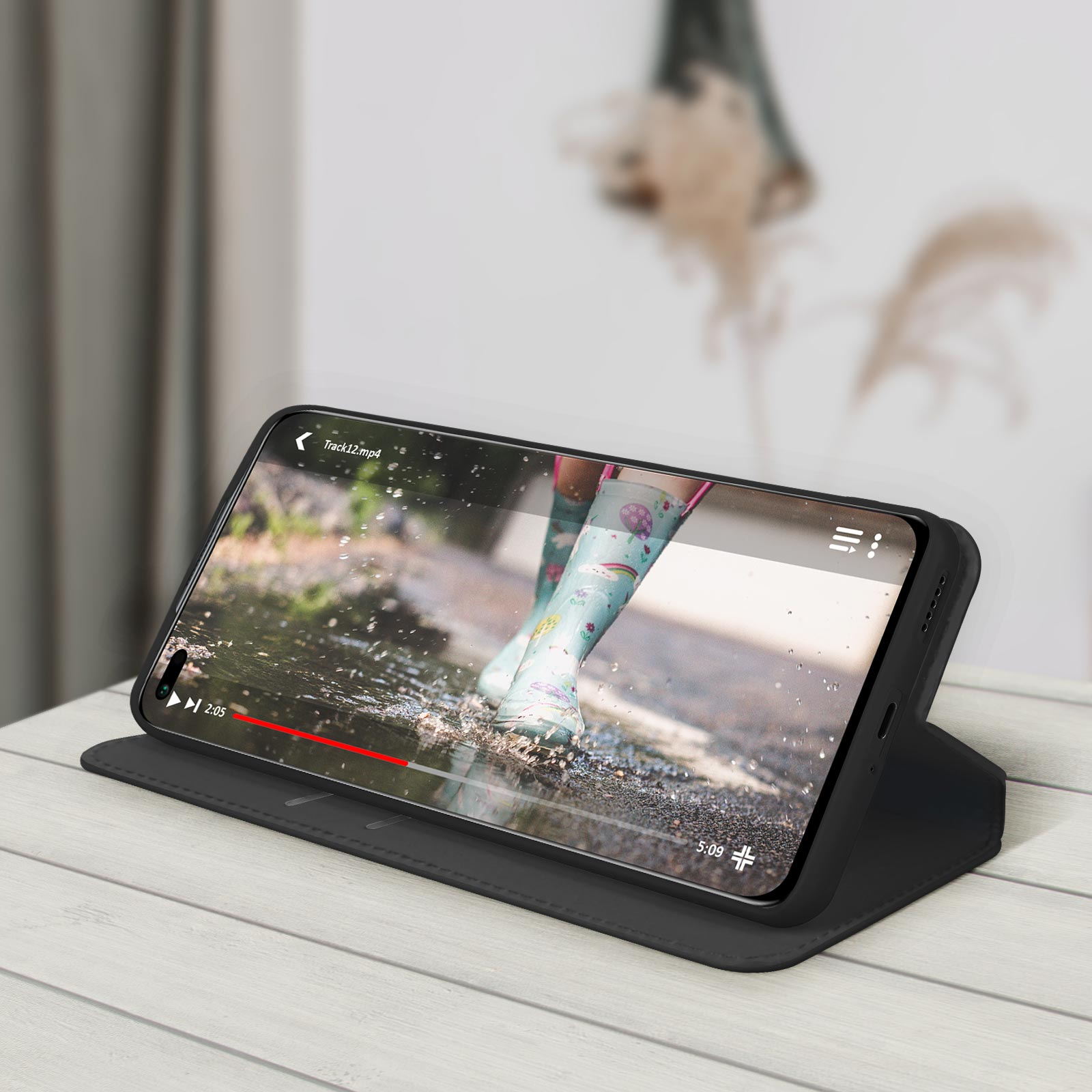 Téléphone dans un étui noir. La vidéo est lue à l'écran. Table blanche et fond flou.