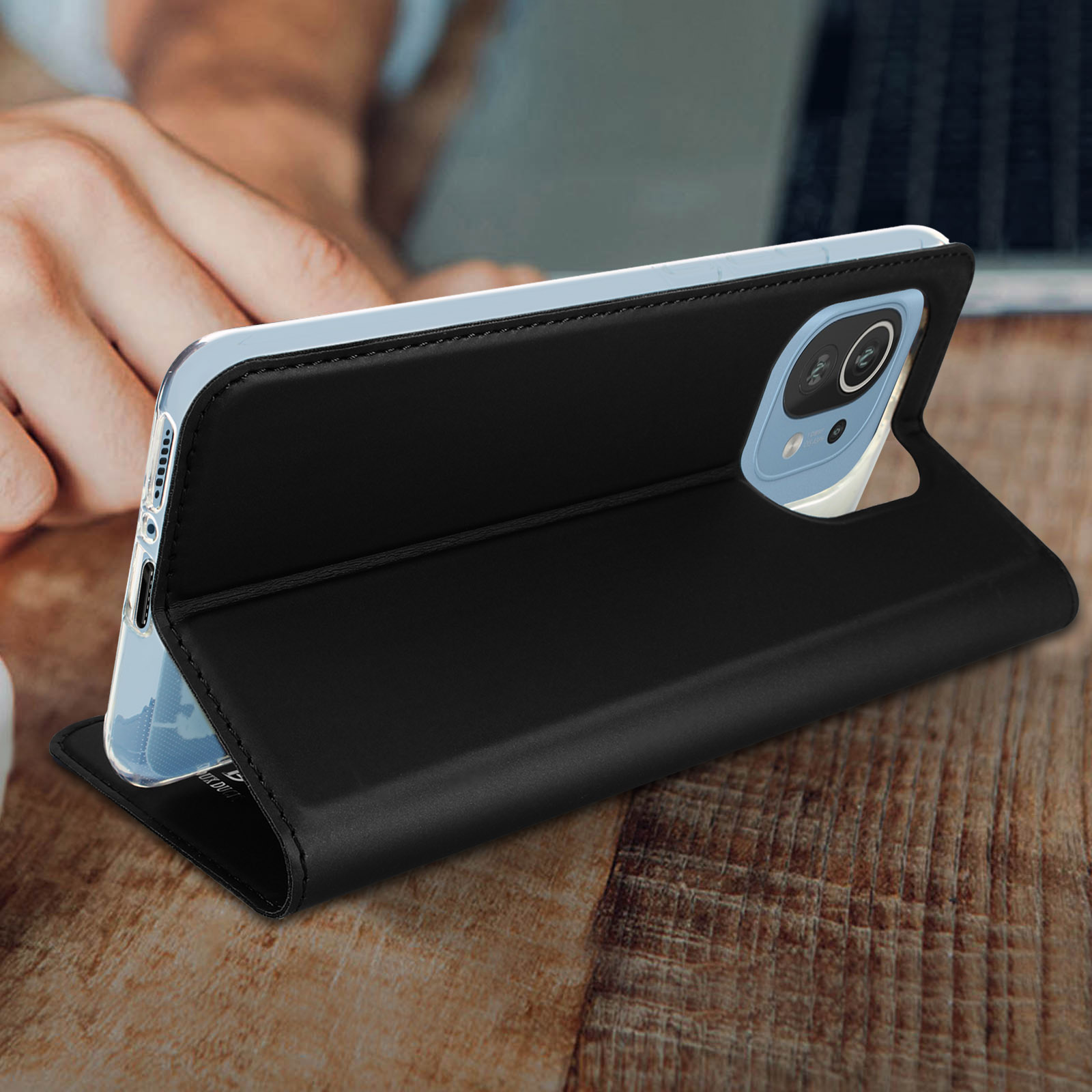 Un telefono in una custodia di pelle nera è aperto su un tavolo di legno. Una mano è visibile.