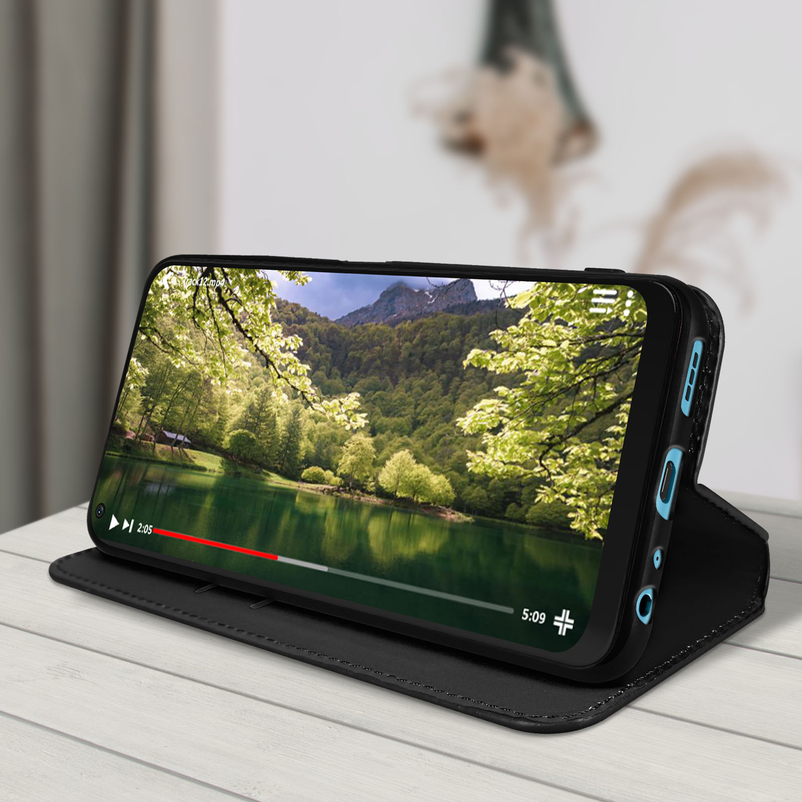 Un telefono in una custodia nera riproduce un video di un lago e montagne, appoggiato su una superficie di legno.