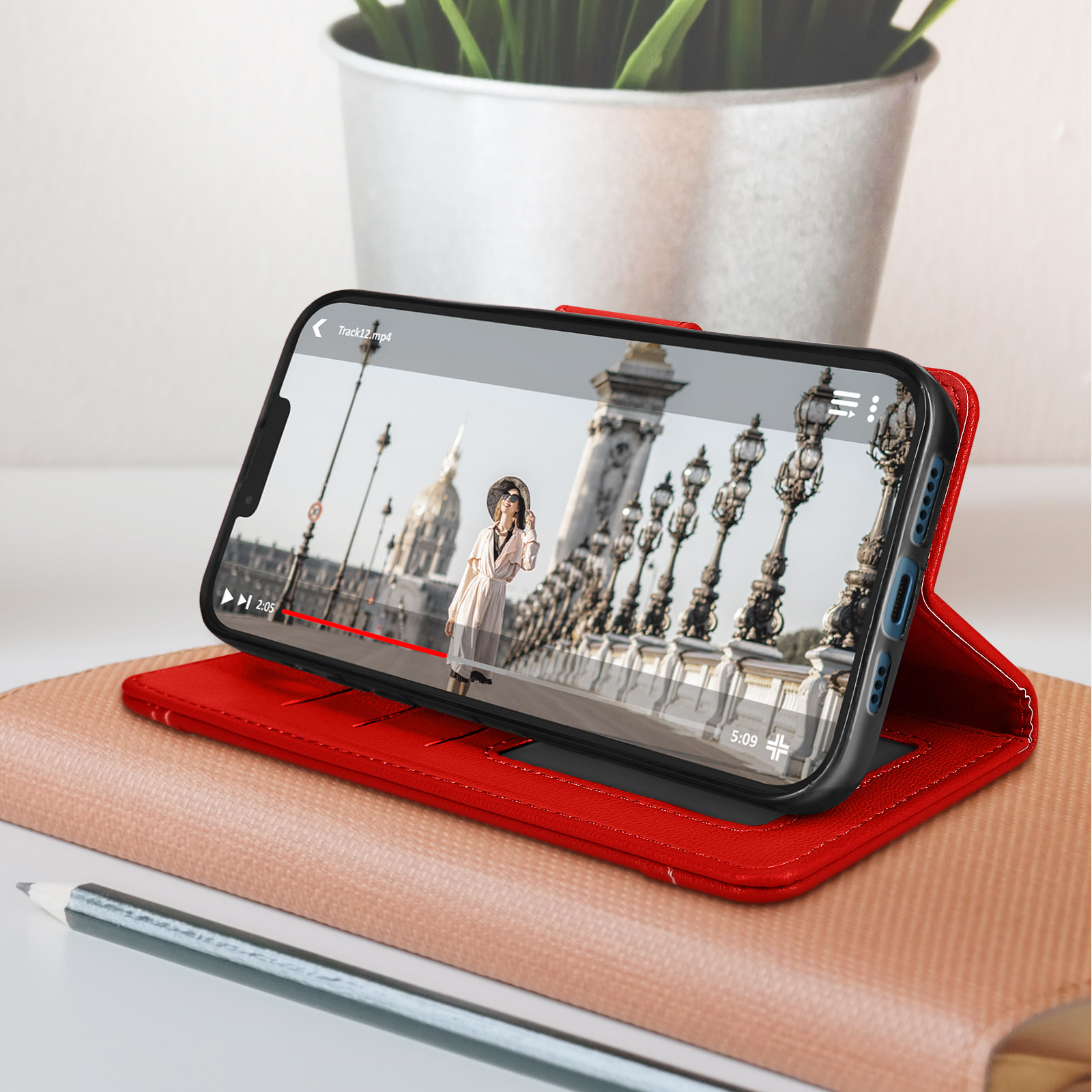 Téléphone dans étui rouge affichant une vidéo, sur étui cuir rouge avec crayon.