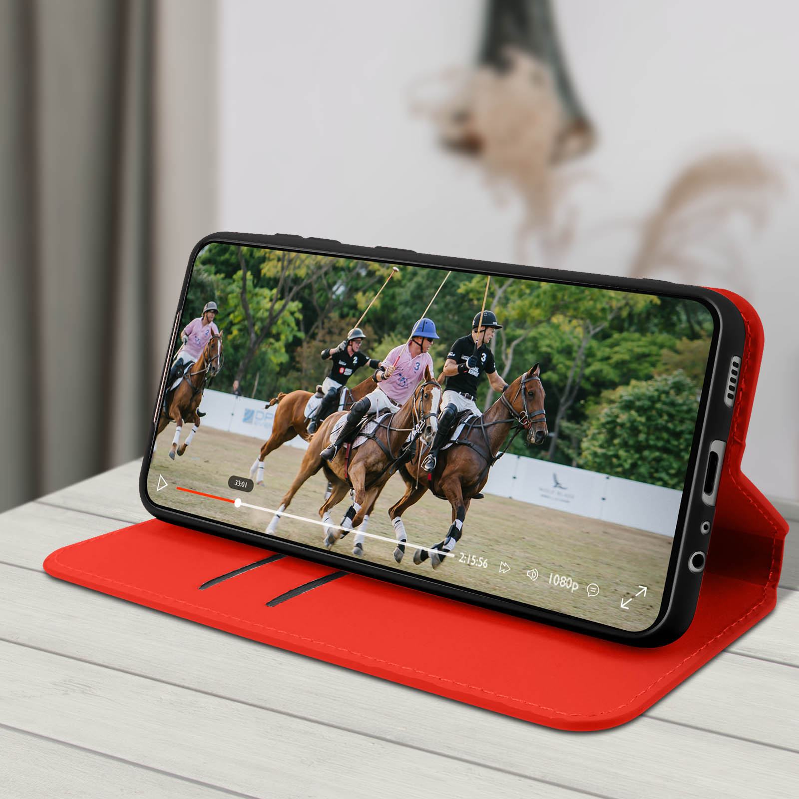 Uno smartphone mostra un video di una partita di polo, posizionato su una custodia protettiva rossa.