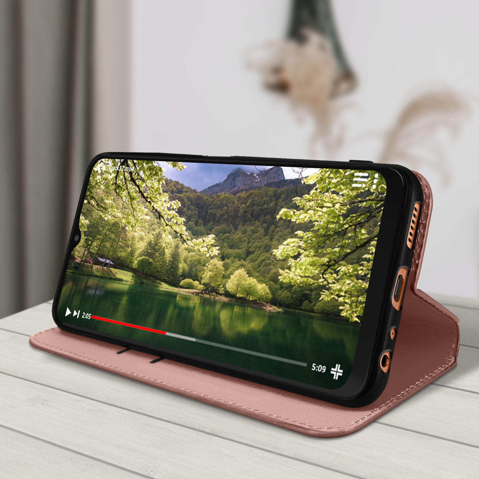 Telefoon in een roze hoes, met een video van een bergmeer op een houten oppervlak.