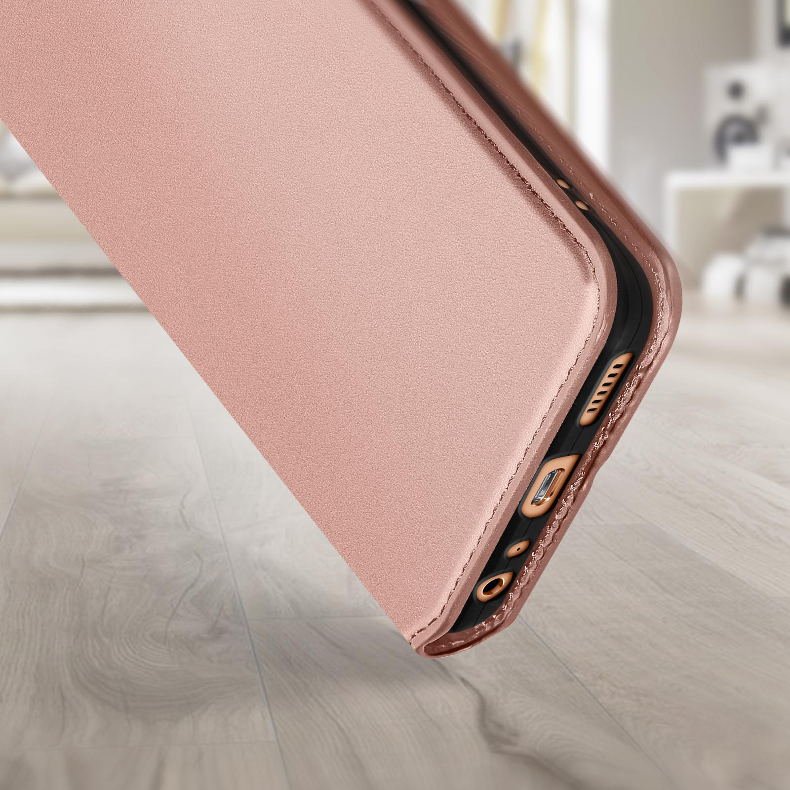 Rosé gouden telefoonhoes, schuin, de onderkant tonend. Houten oppervlak, wazige achtergrond.