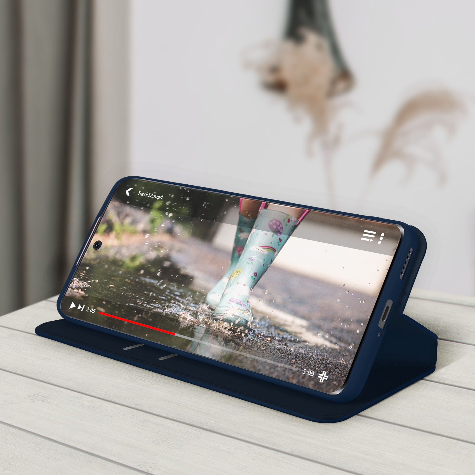 Telefono in una custodia blu, che mostra un video di bambini con stivali da pioggia. Su una superficie di legno.