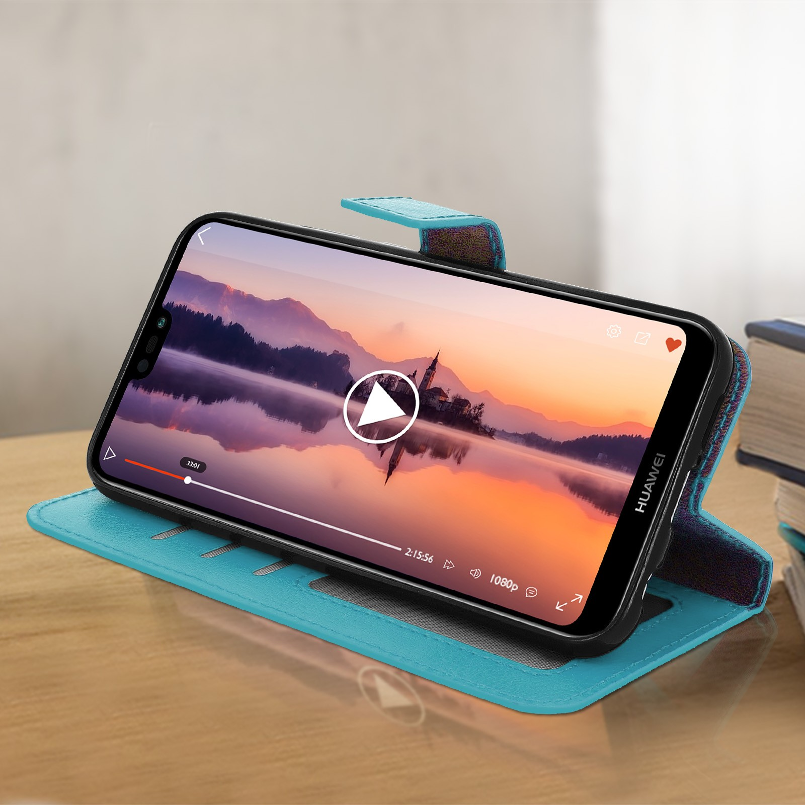 Un telefono con un video in riproduzione su una custodia blu, su una scrivania di legno con libri.