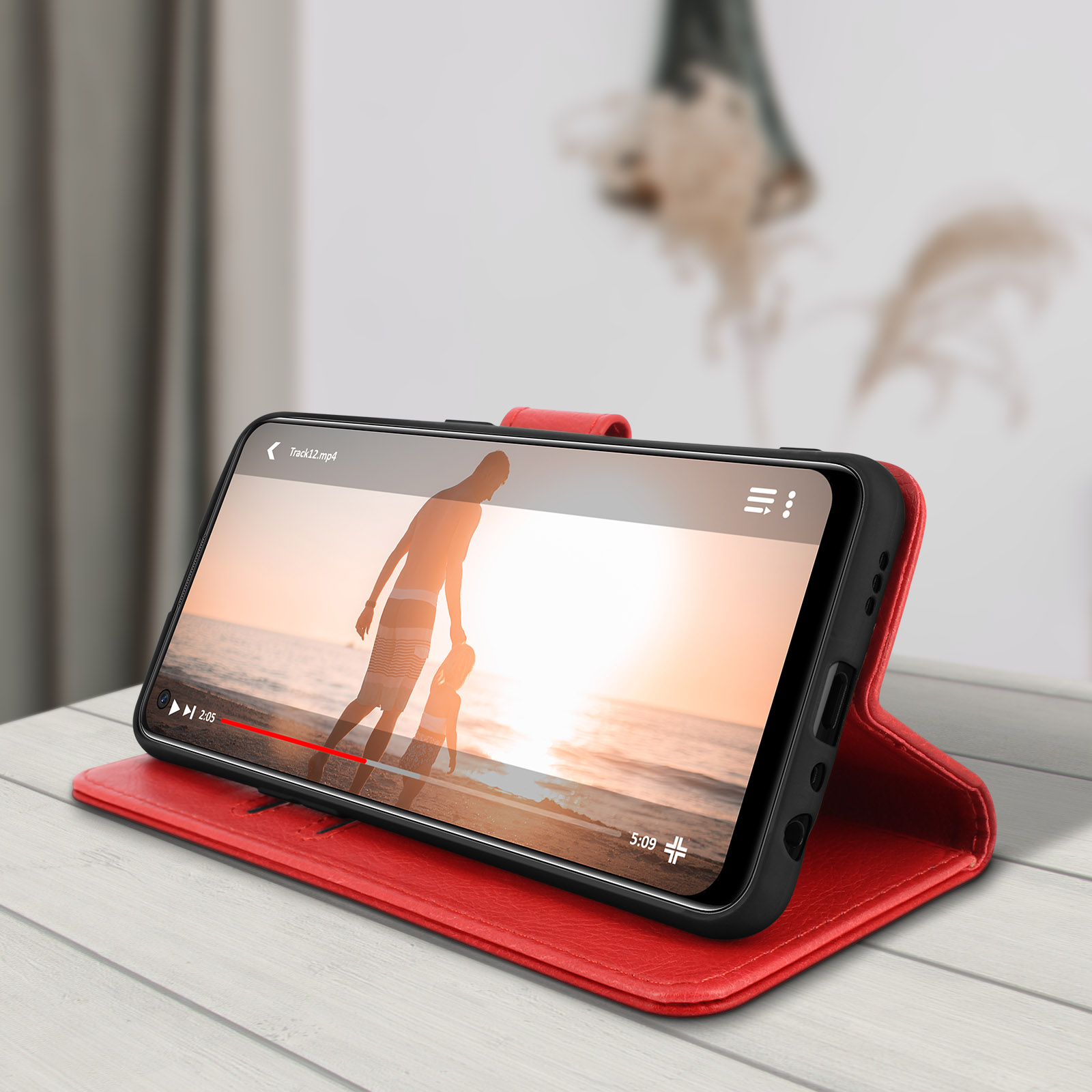 Étui de téléphone en cuir rouge, ouvert, avec vidéo sur le téléphone. Table en bois. Arrière-plan flou d'une pièce.
