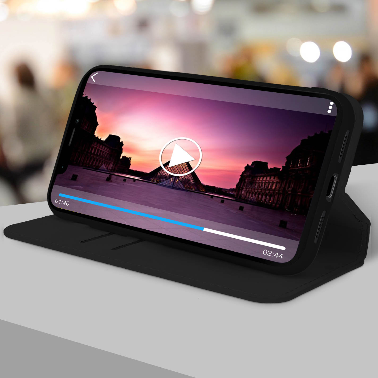 Telefono in una custodia nera che mostra un video, con il Louvre sullo sfondo.