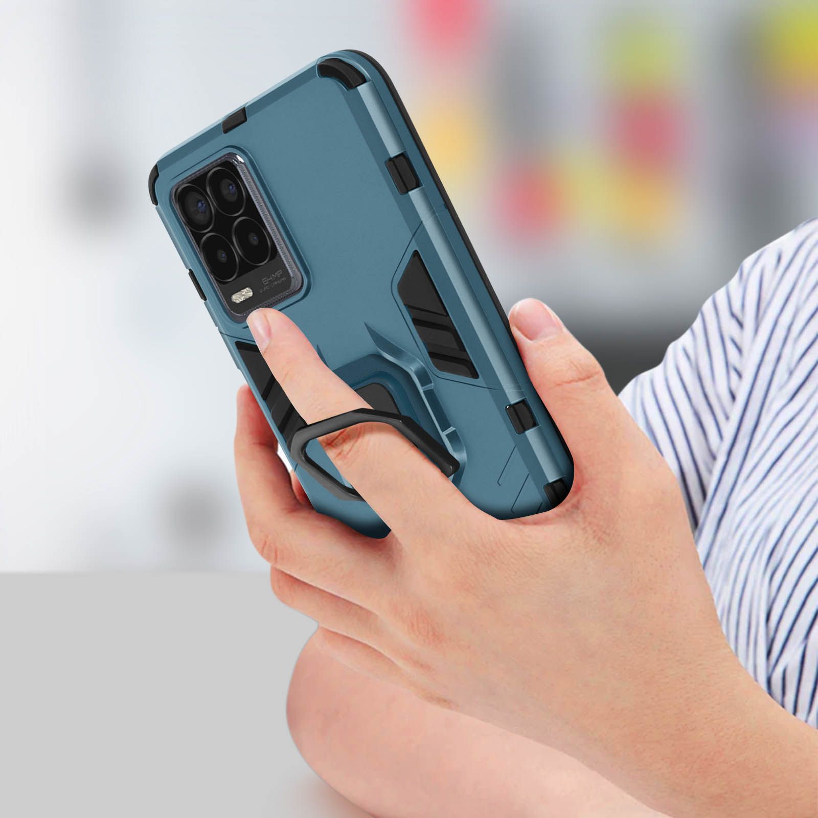 Persona che tiene un telefono con custodia blu. Il telefono ha un supporto ad anello. Sfondo a righe.